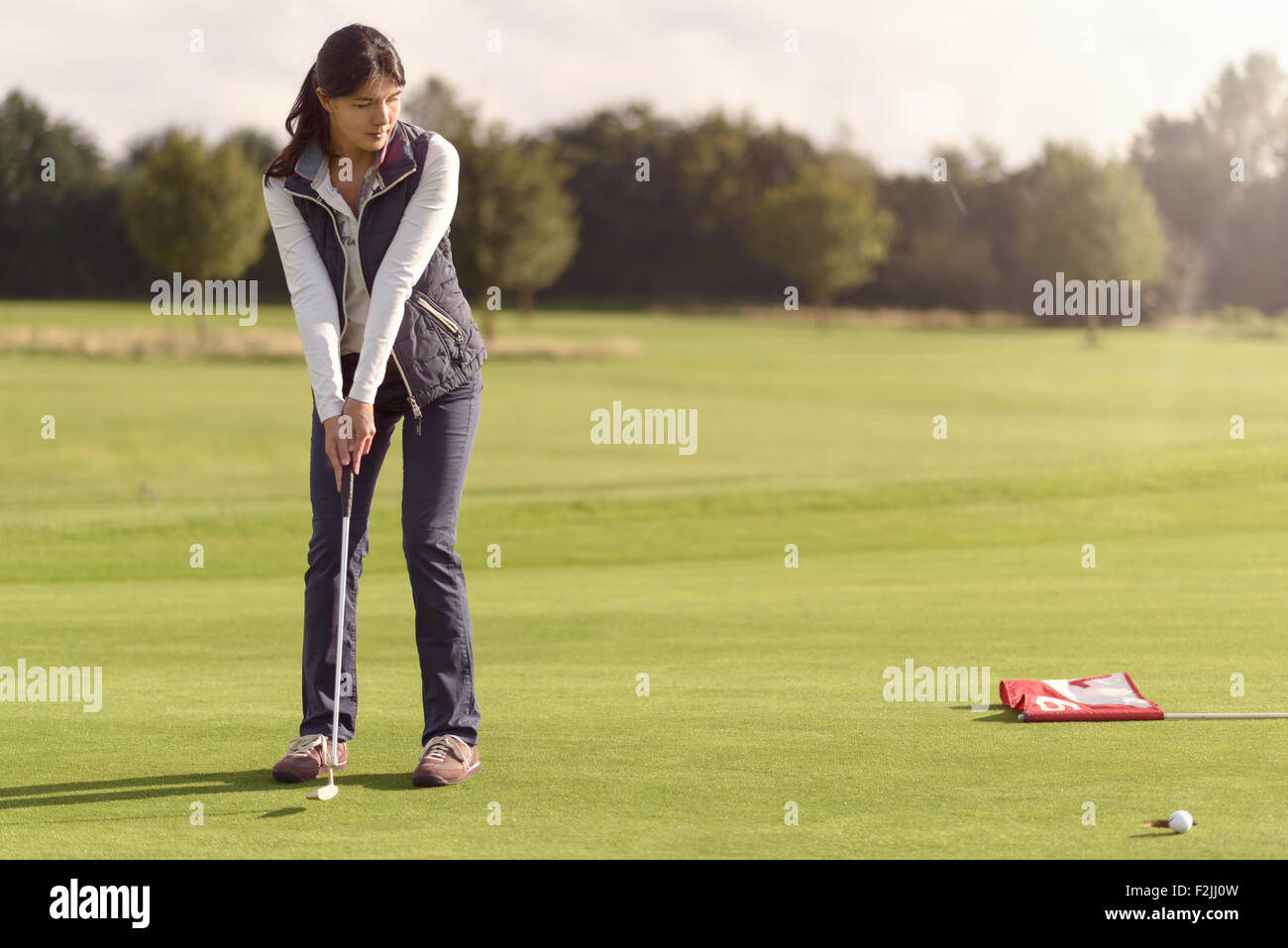 Attraente golfista femmina messa per il foro sul verde utilizzando un putter e guardare la pallina da golf rotolo verso la coppa Foto Stock