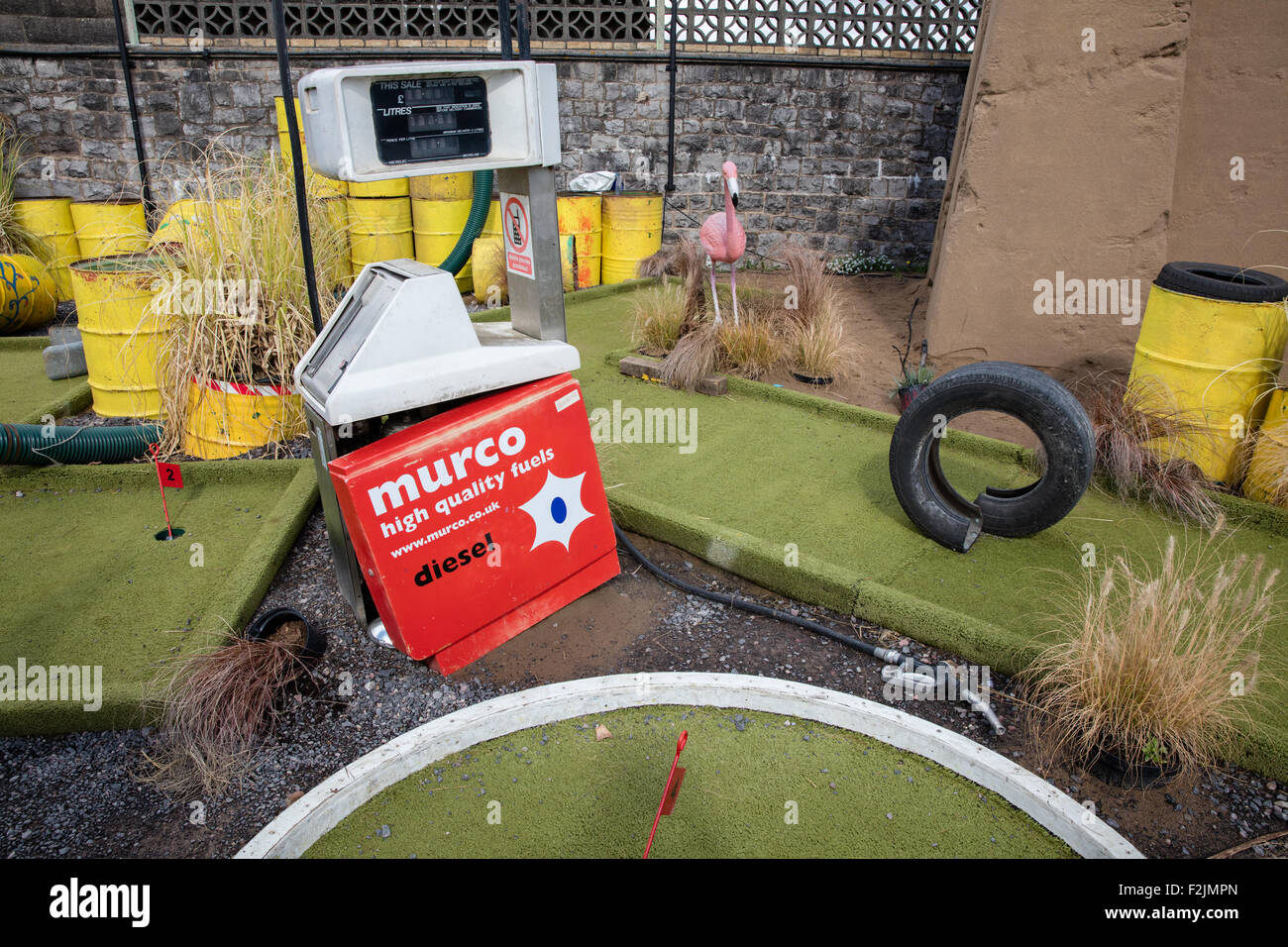 Crazy Golfo di corso presso Banksy's Dismaland in Weston super Mare con martoriata pompa carburante di fusti di olio e vecchi pneumatici plus fenicottero rosa Foto Stock