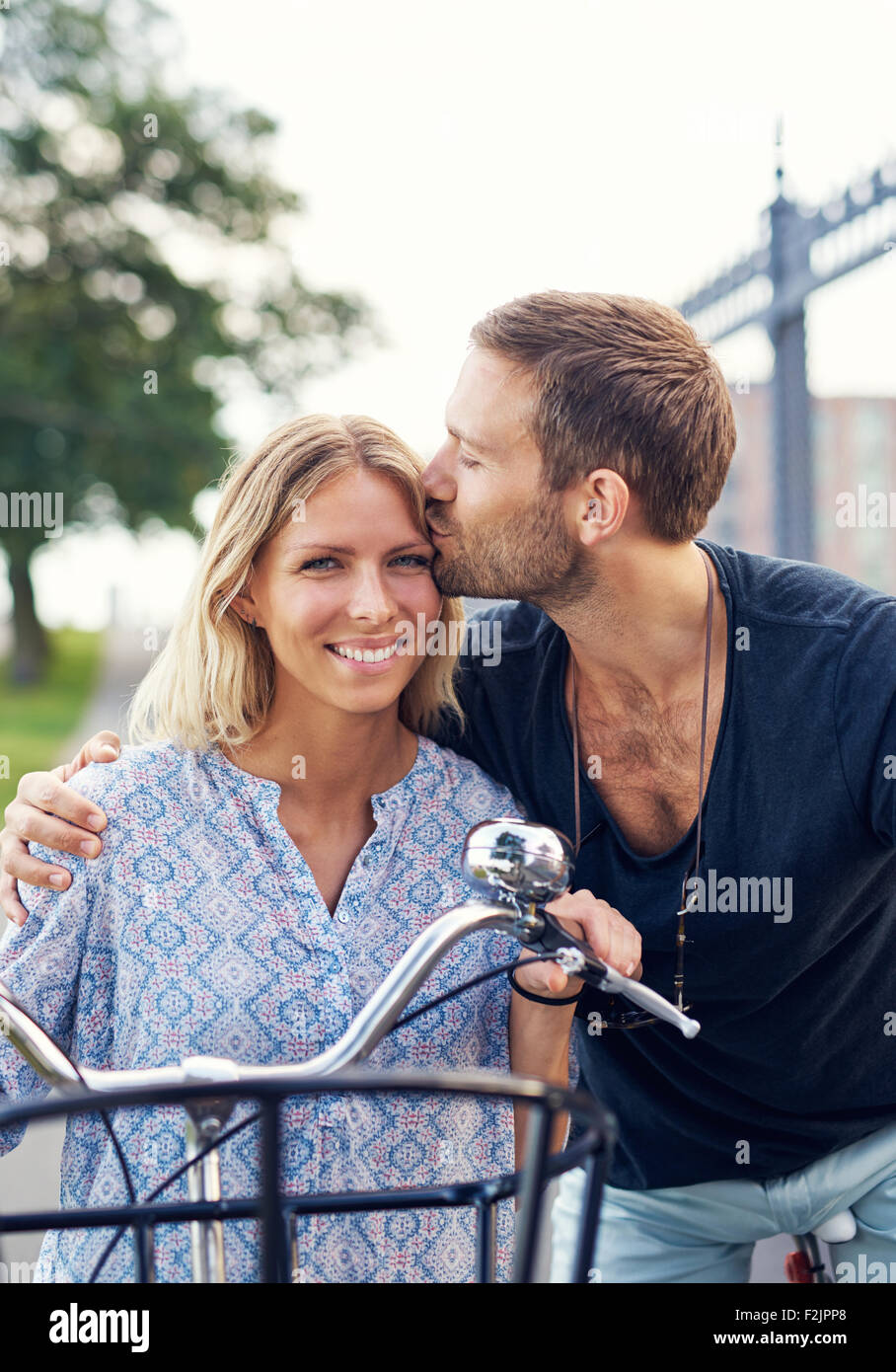 Affettuosa giovane baciare la sua ragazza sulla fronte come essi godono di un giorno di estate in aria fresca sui loro biciclette Foto Stock
