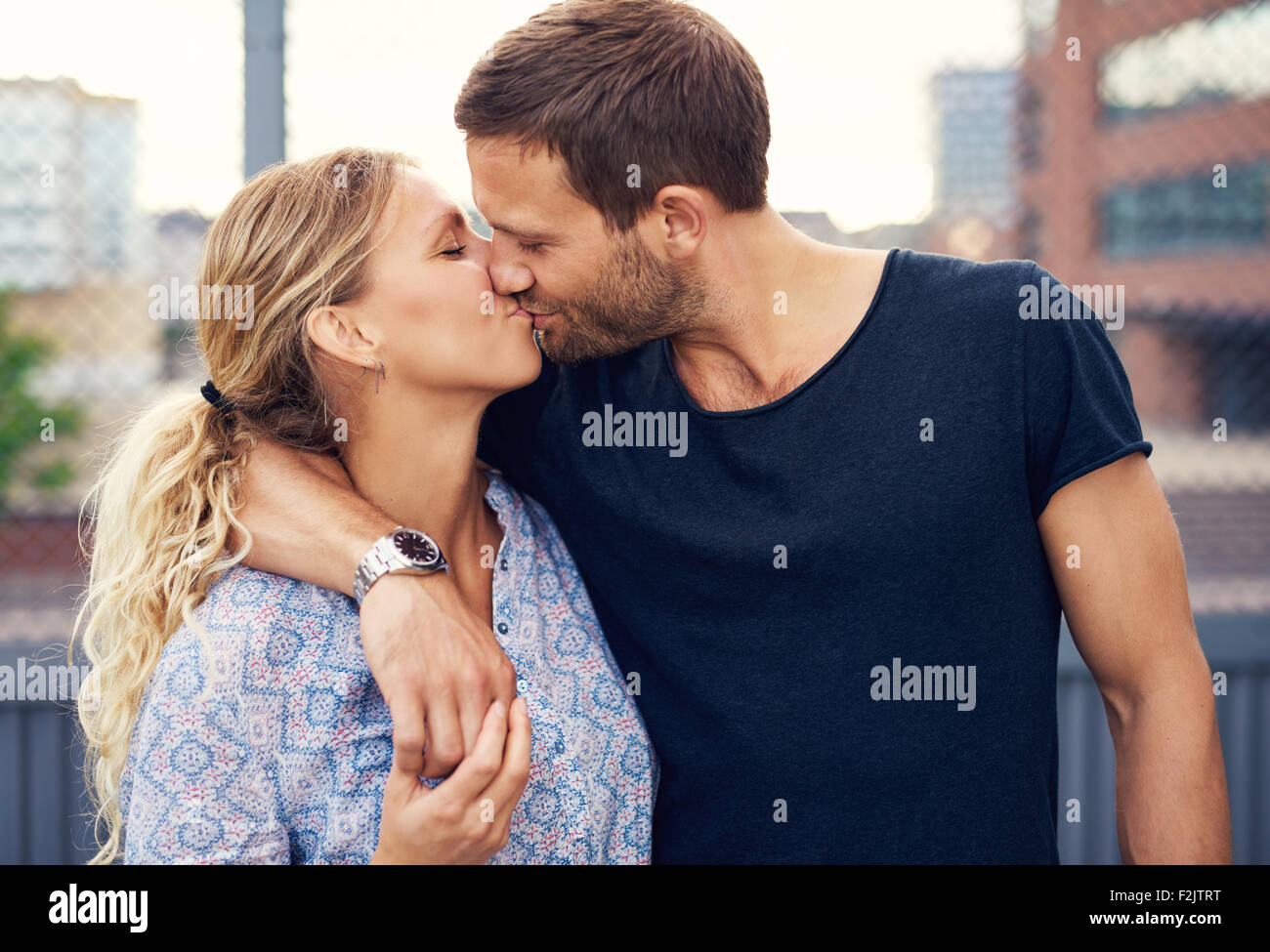 Attraente amorosa coppia giovane godetevi una romantica bacio come stanno a braccetto all aperto in una strada urbana Foto Stock