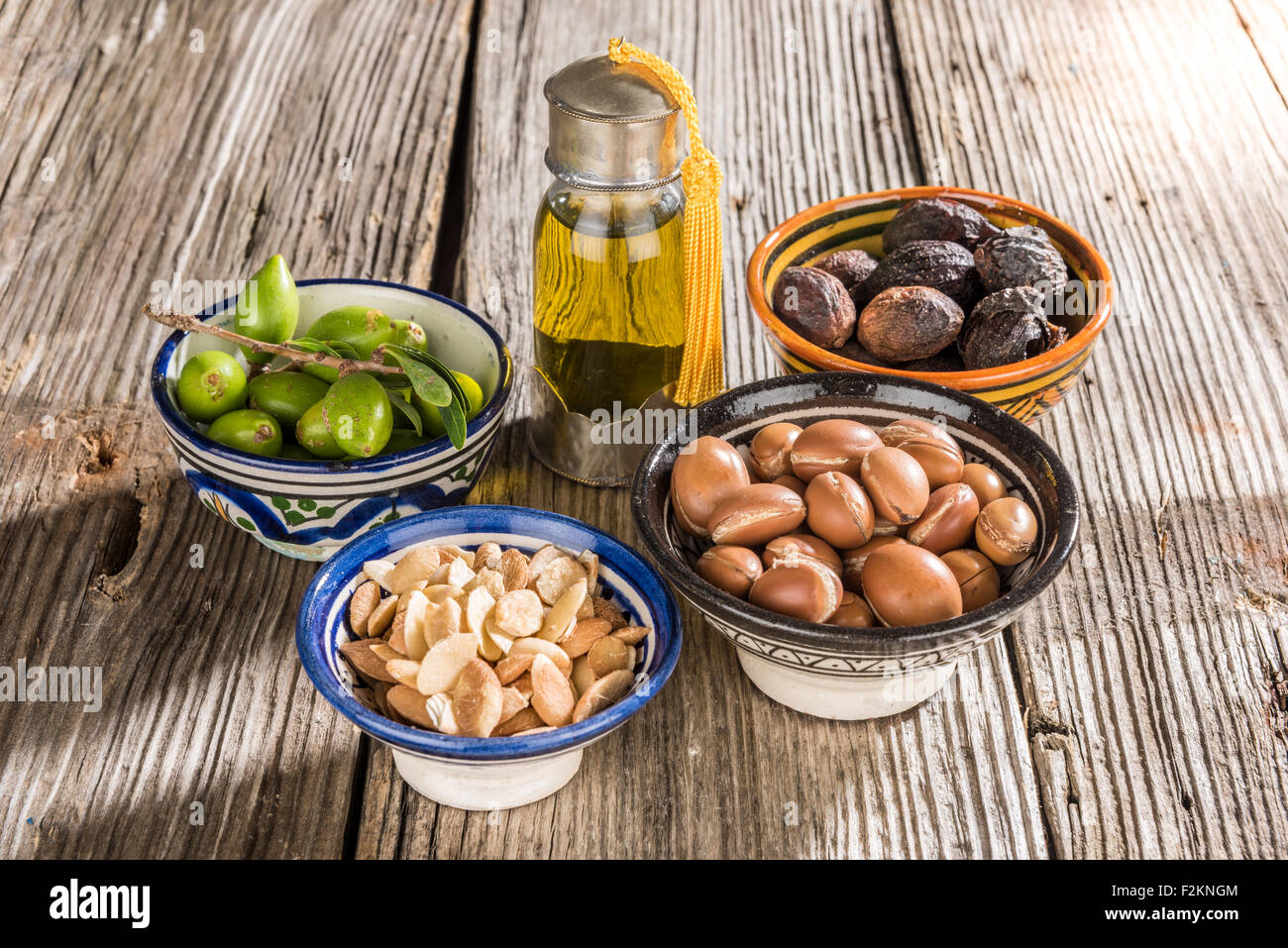 Frutti di Argan su un tavolo di legno, alcuni frutti sono senza guscio, altri sono in un tajine marocchino Foto Stock