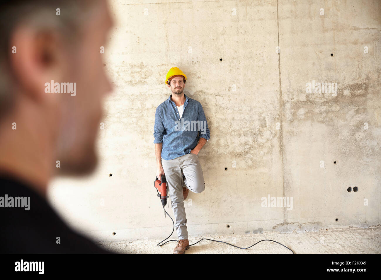 Uomo con elmetto site permanente al muro di cemento azienda drill Foto Stock