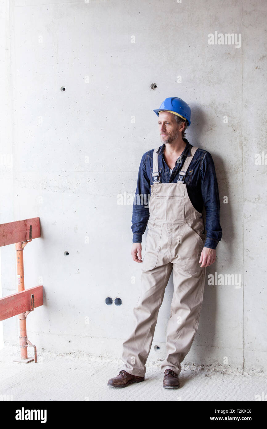 Lavoratore sul sito in costruzione permanente al muro di cemento Foto Stock