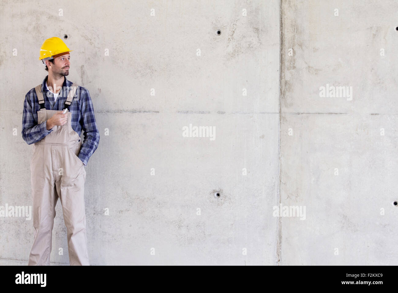 Uomo con il casco sul sito in costruzione a parete in calcestruzzo Foto Stock