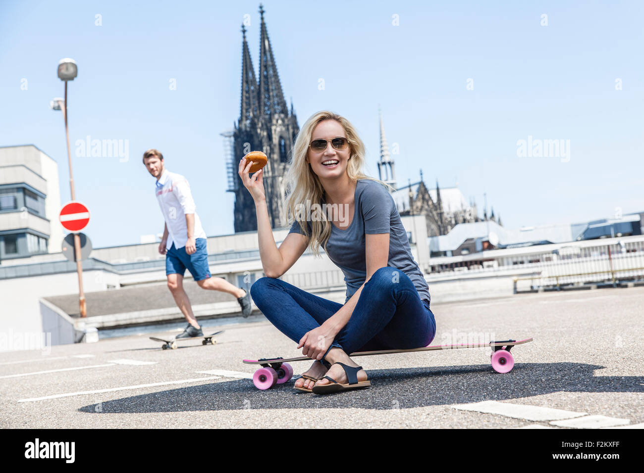 Germania, Colonia, Ritratto di giovane donna con bagel seduto su skateboard Foto Stock
