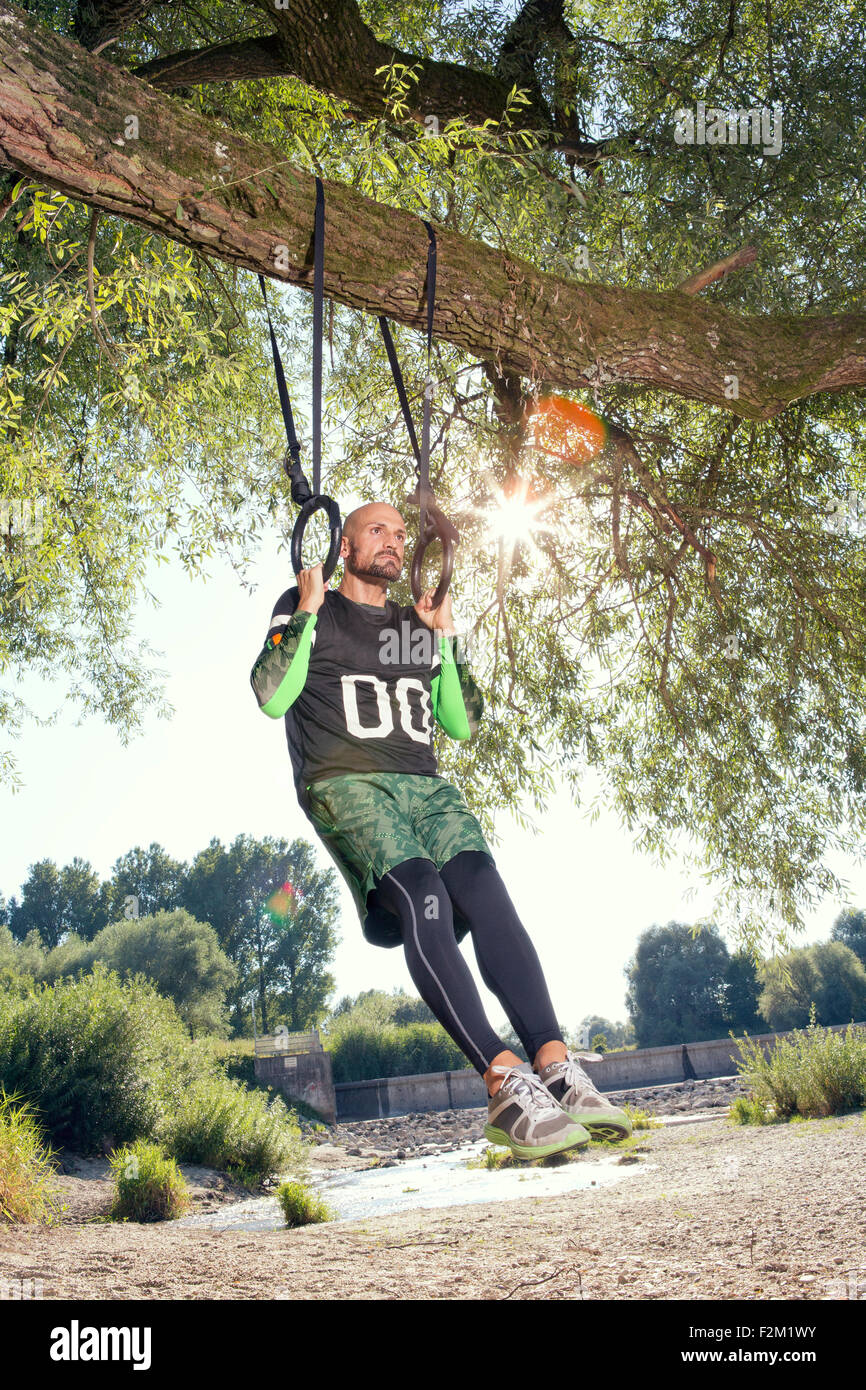 L'uomo facendo esercizio CrossFit sugli anelli appesi a tronco di albero Foto Stock