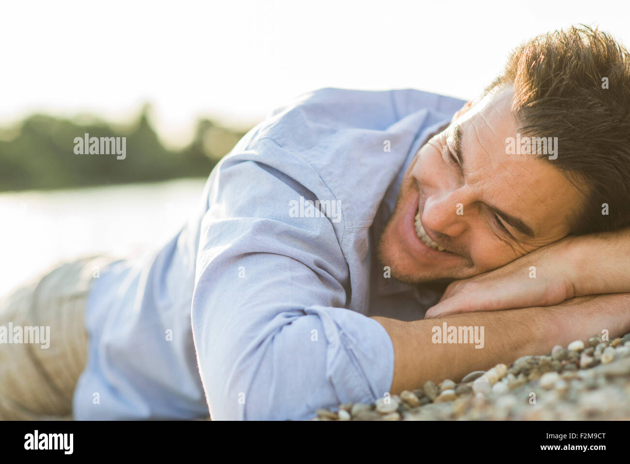 Uomo sorridente che giace sulla spiaggia sassosa al crepuscolo serale Foto Stock