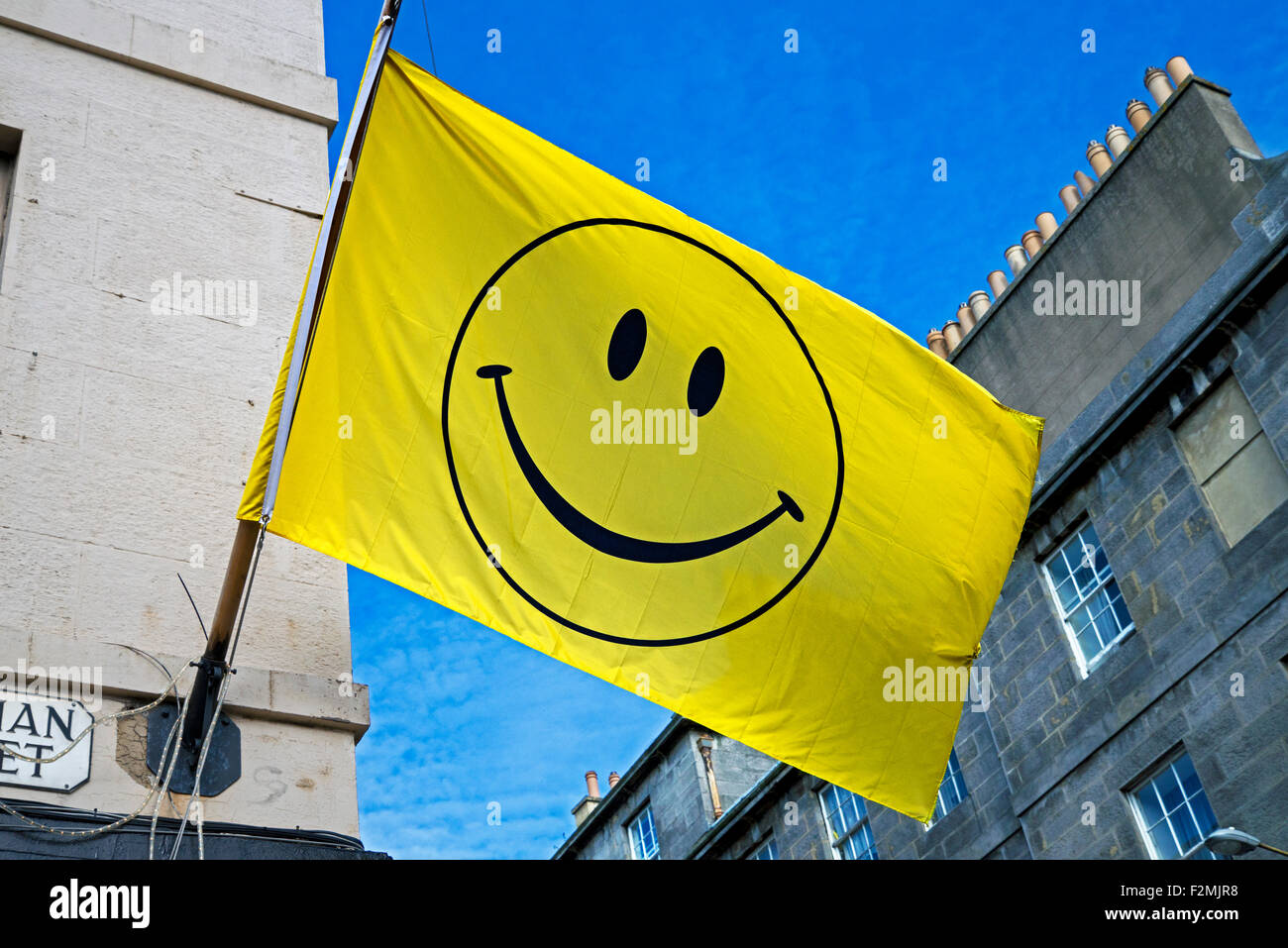 Una faccina sorridente su una bandiera gialla contro un cielo blu di Edimburgo. Foto Stock