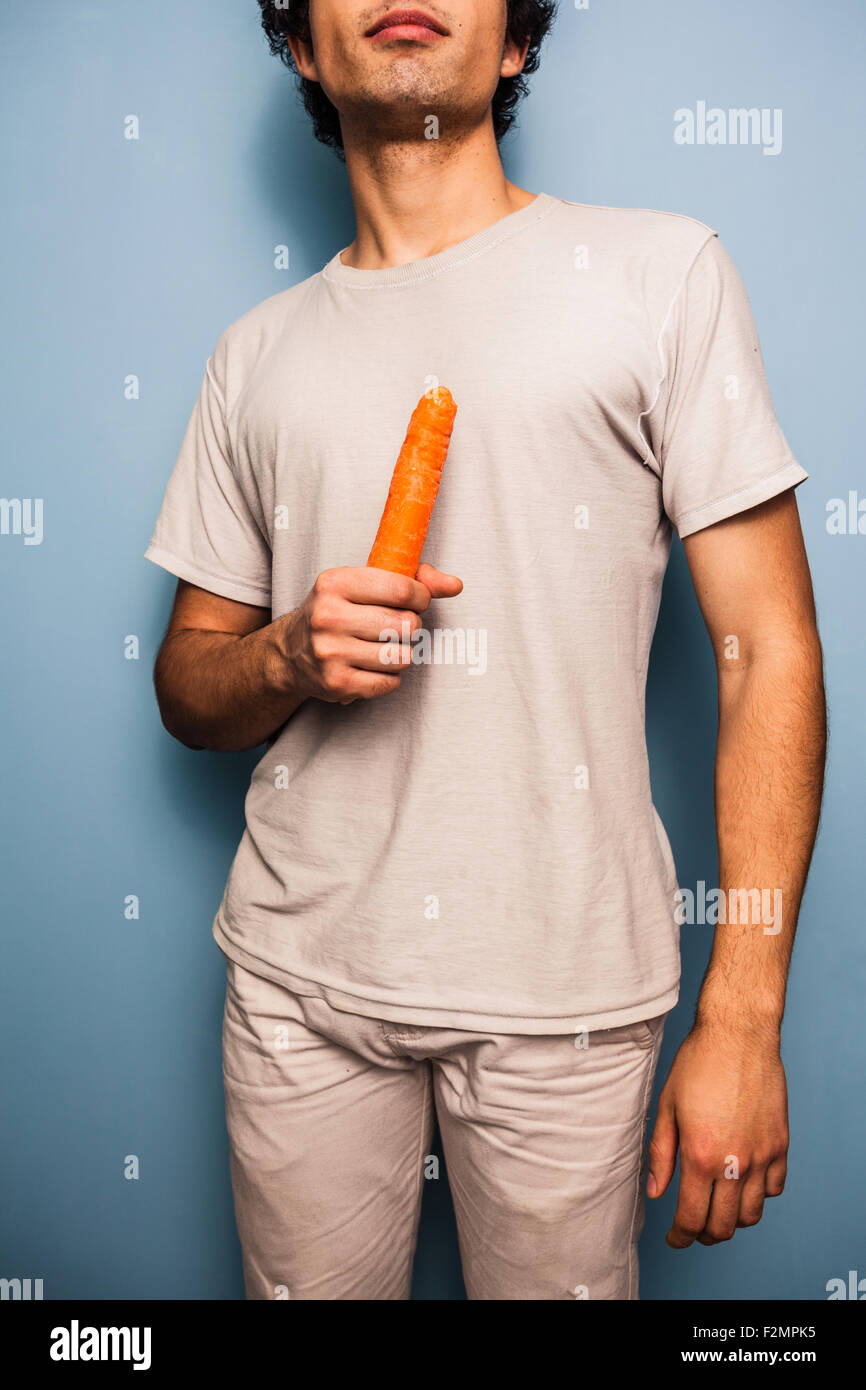 Giovane uomo in piedi da una parete blu con una carota Foto Stock