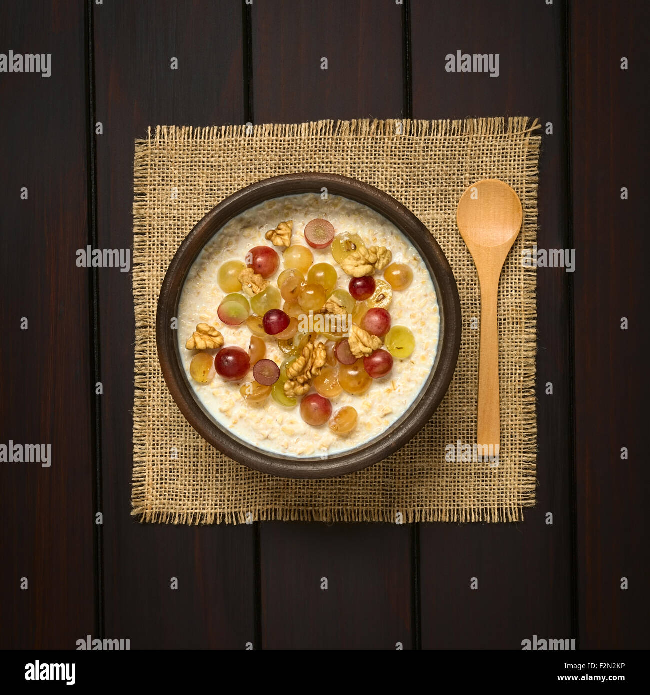 Farina di avena porridge con uva e noci nella ciotola rustico, il cucchiaio di legno sul lato Foto Stock
