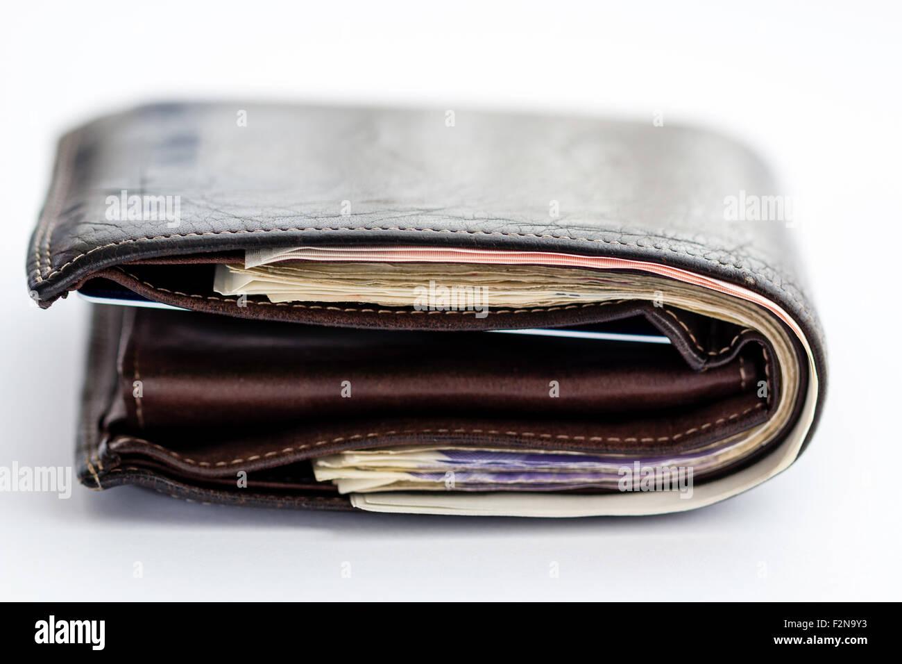 Ripiegate in pelle marrone scura stipati a portafoglio con banconote su sfondo bianco. Foto Stock