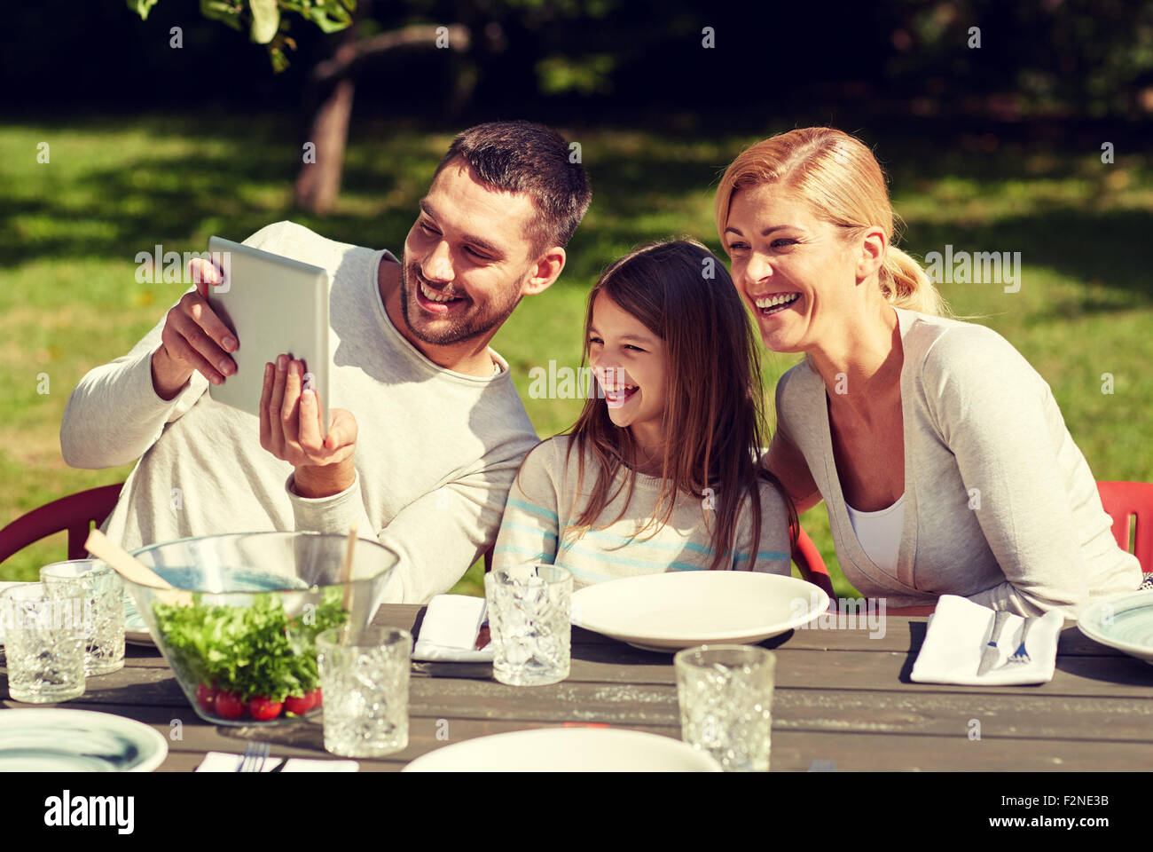 La famiglia felice con il tablet pc al tavolo in giardino Foto Stock