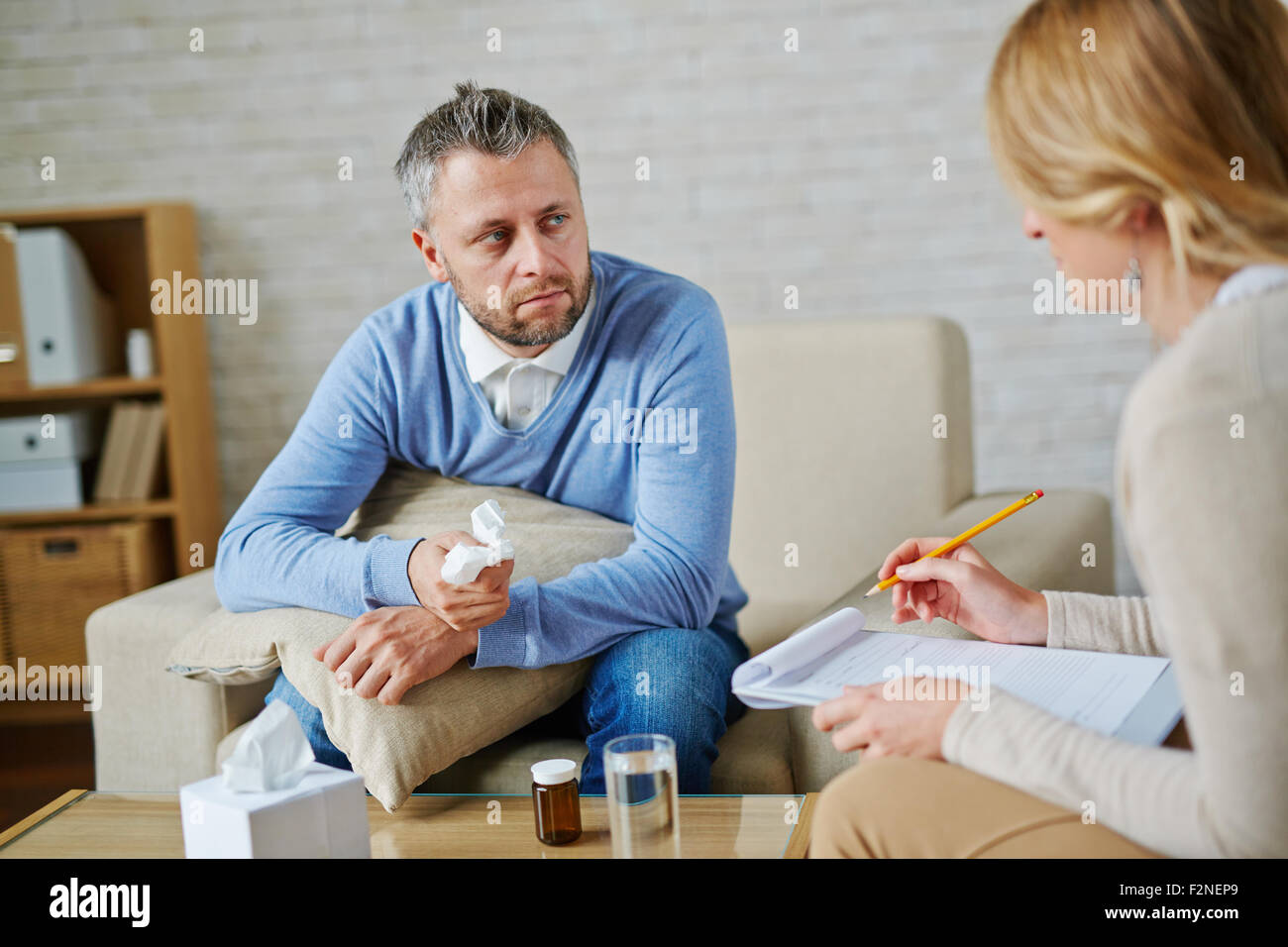 Uomo disperato con cuscino e fazzoletto guardando al suo psicologo durante la consultazione Foto Stock