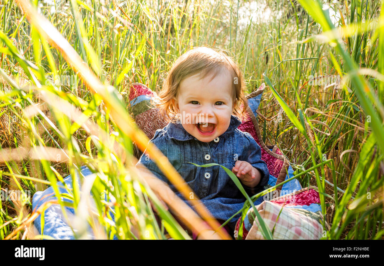Caucasian baby ragazza seduta in erba alta Foto Stock