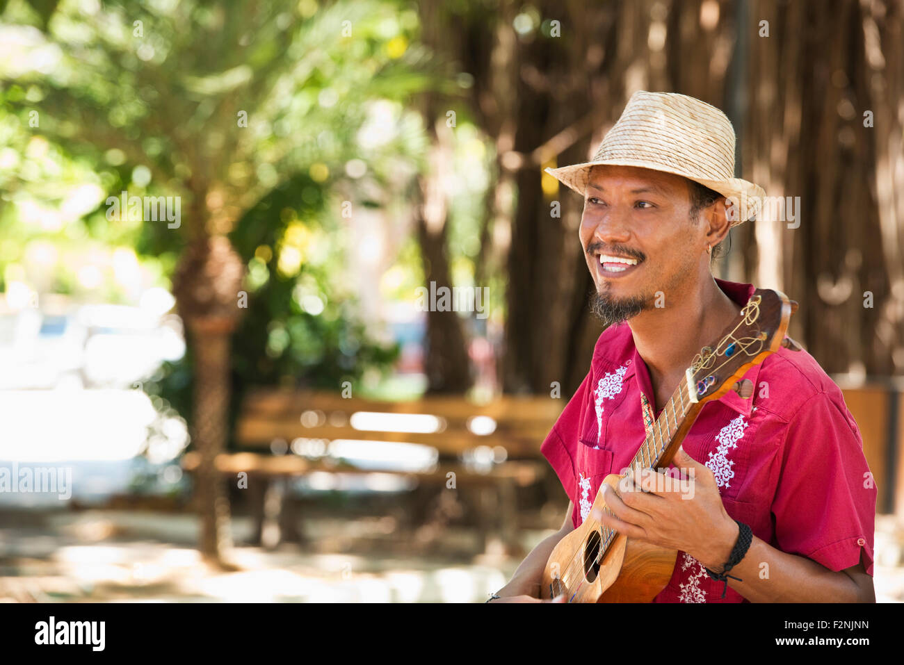 Musicista di origine ispanica giocando ukulele in posizione di parcheggio Foto Stock
