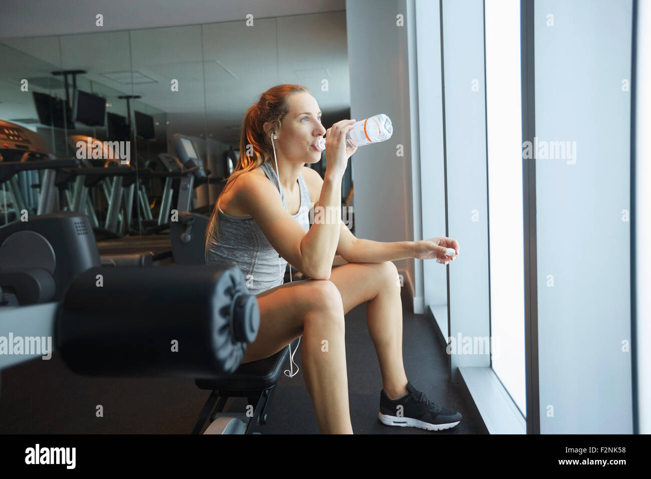 Donna di bere acqua in bottiglia in palestra Foto Stock