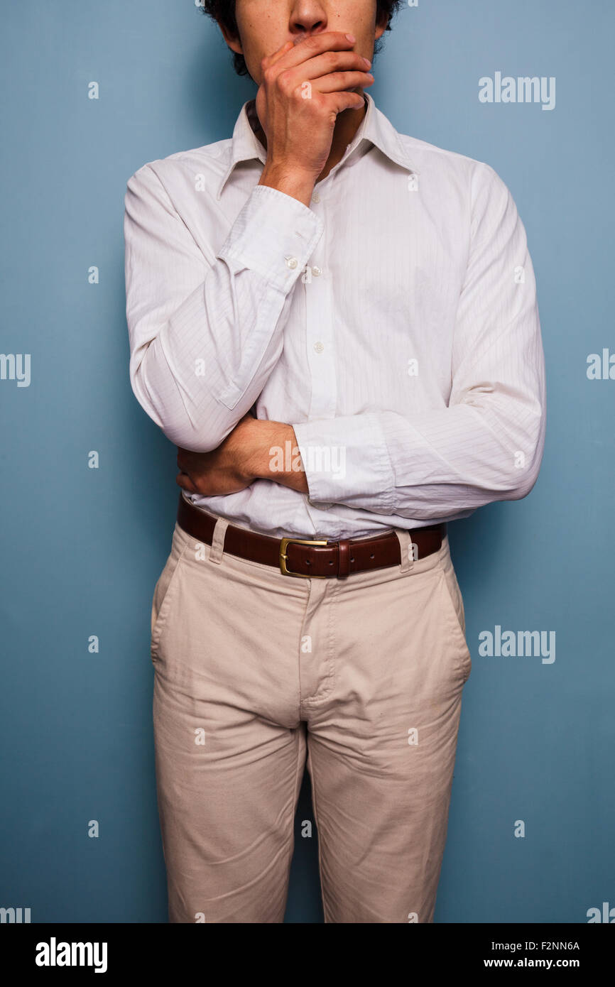 Giovane uomo in piedi da una parete blu con la sua mano sulla sua bocca Foto Stock