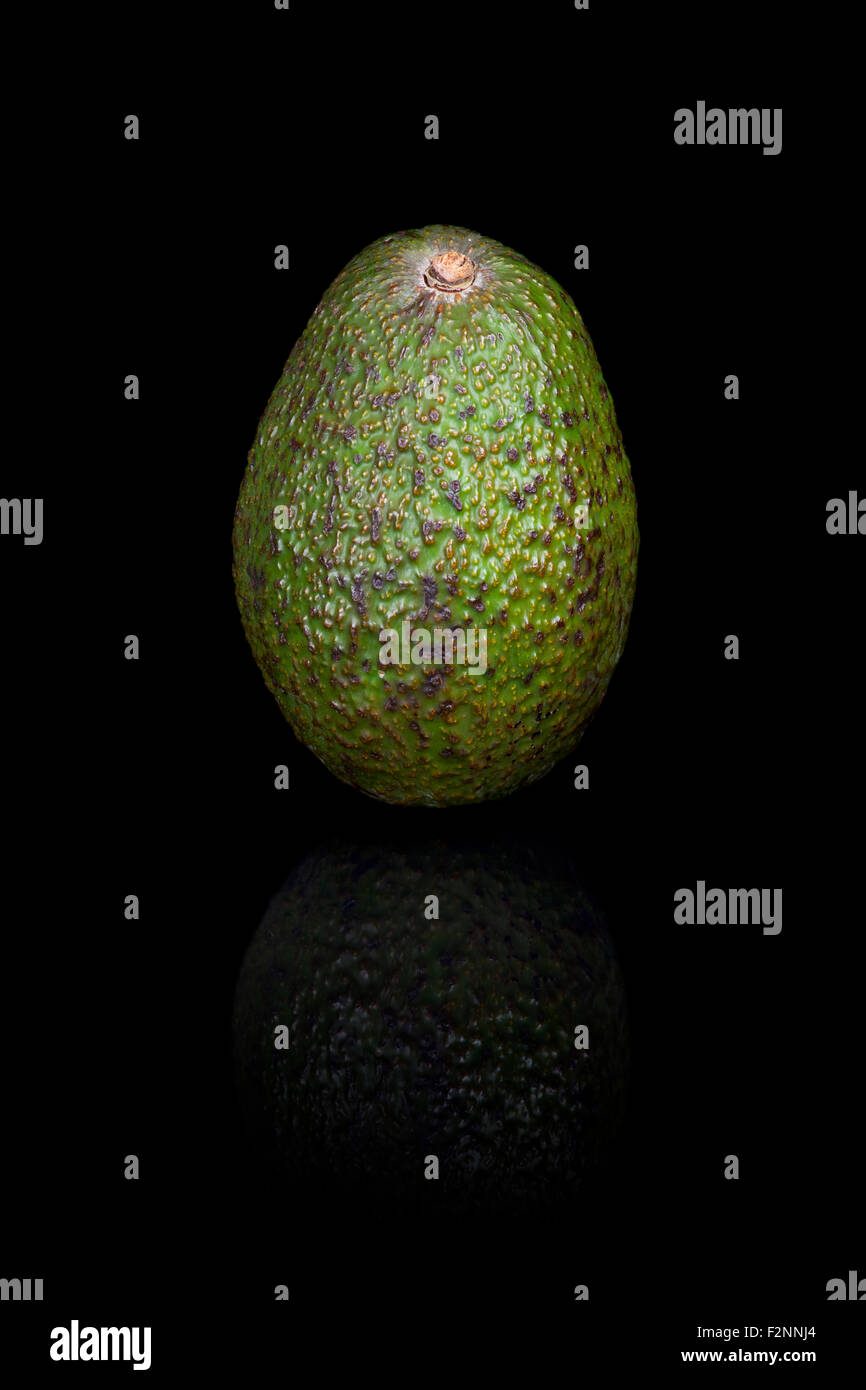 Un avocado su un nero sfondo riflettente. Foto Stock