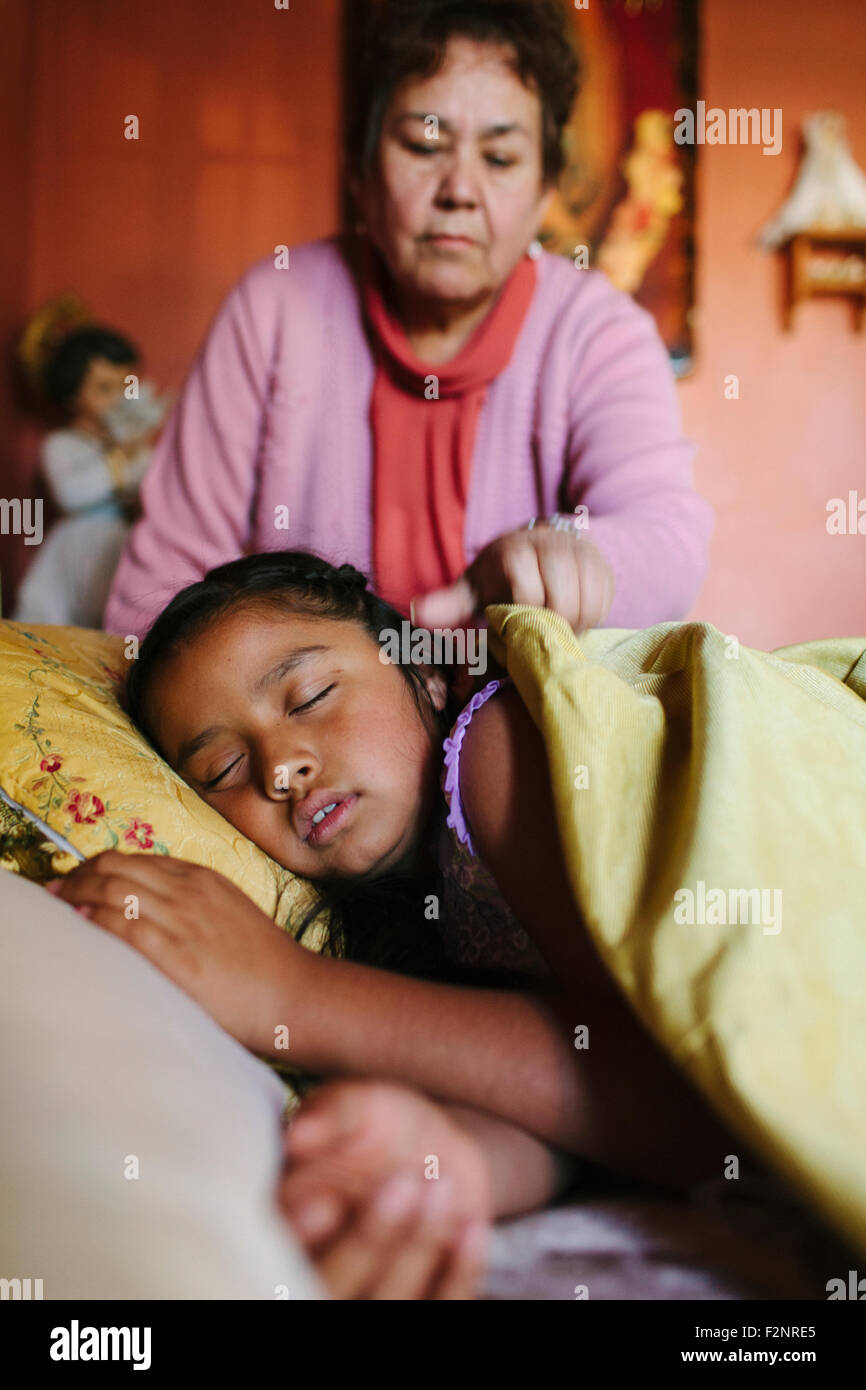 Nonna ispanica rimboccandosi nipote in letto Foto Stock