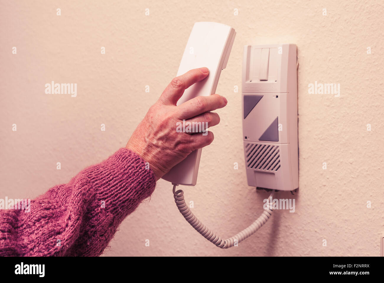 Una donna matura è il prelievo di un interfono ricevitore telefonico da una unità montata a parete. Foto Stock