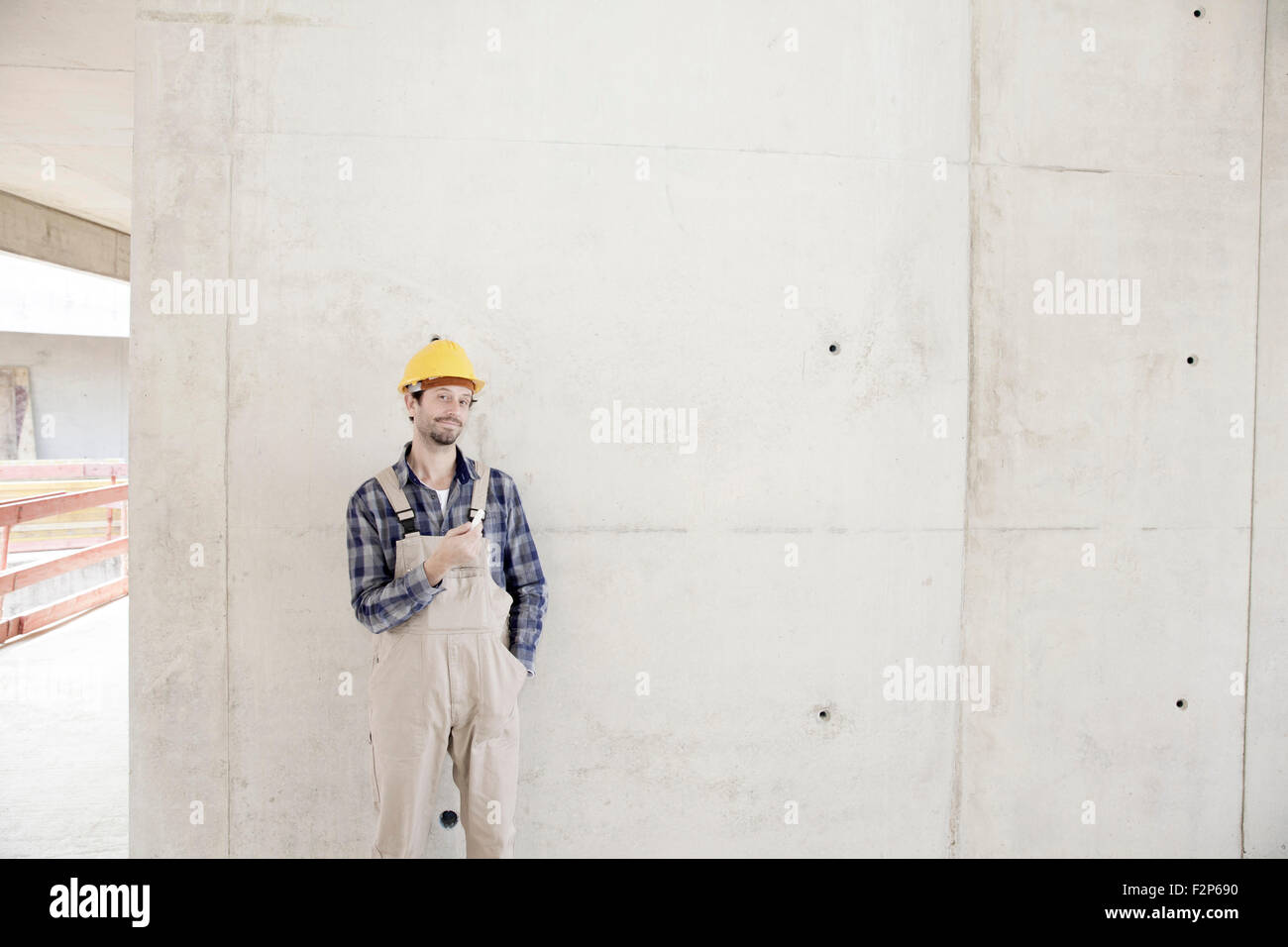 Uomo con il casco sul sito in costruzione a parete in calcestruzzo Foto Stock