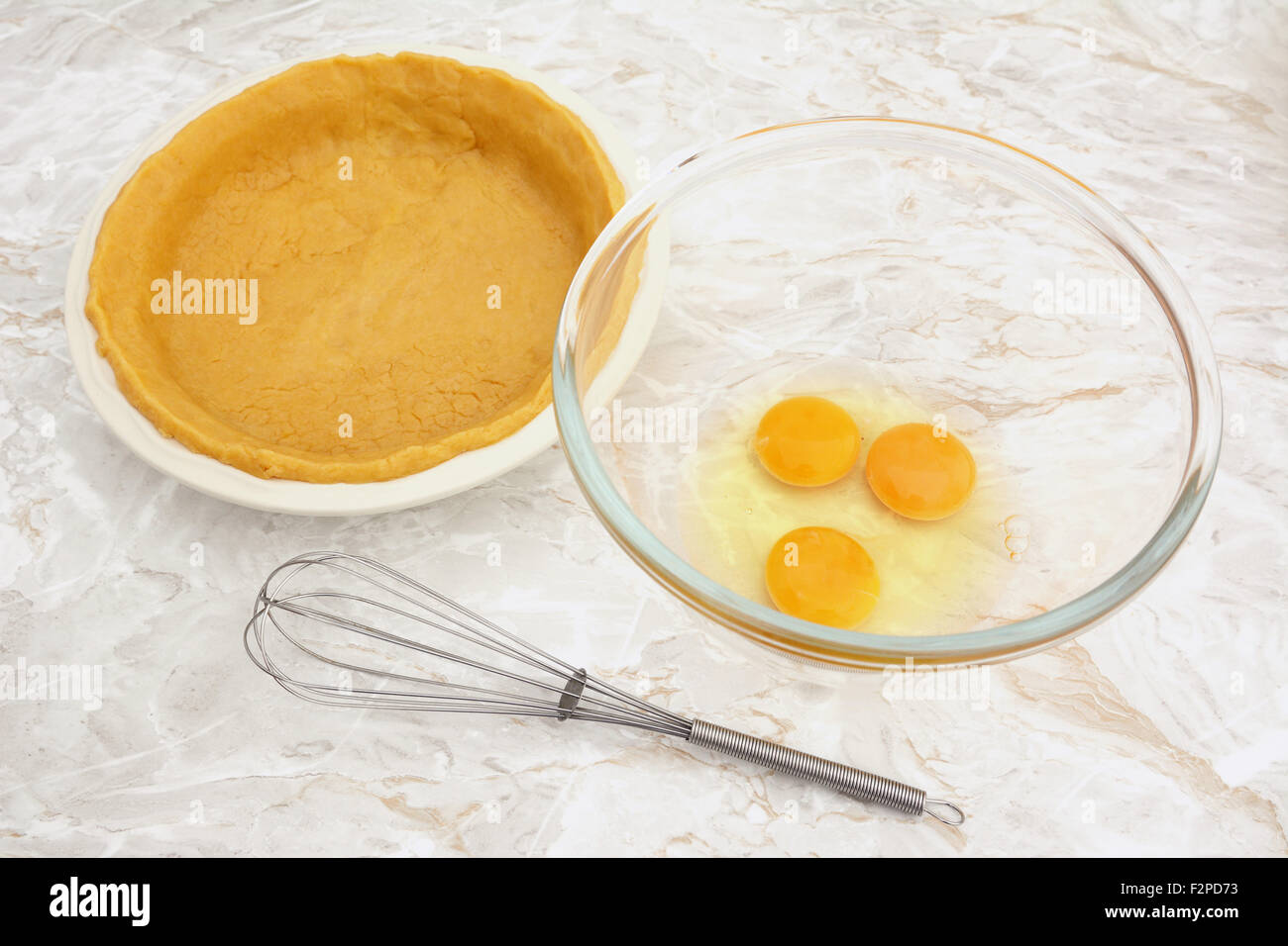 Ciotola di uova crude con una frusta e una teglia foderata con pasta frolla Foto Stock