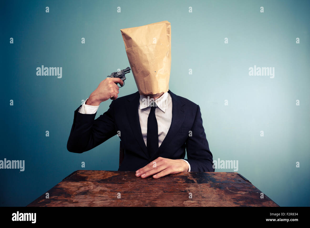 Imprenditore con sacchetto di carta sopra la sua testa di suicidarsi sparando se stesso Foto Stock