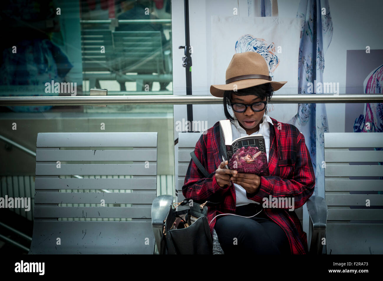 Una giovane femmina nero la lettura di un libro, la stazione di Waterloo, Londra Foto Stock