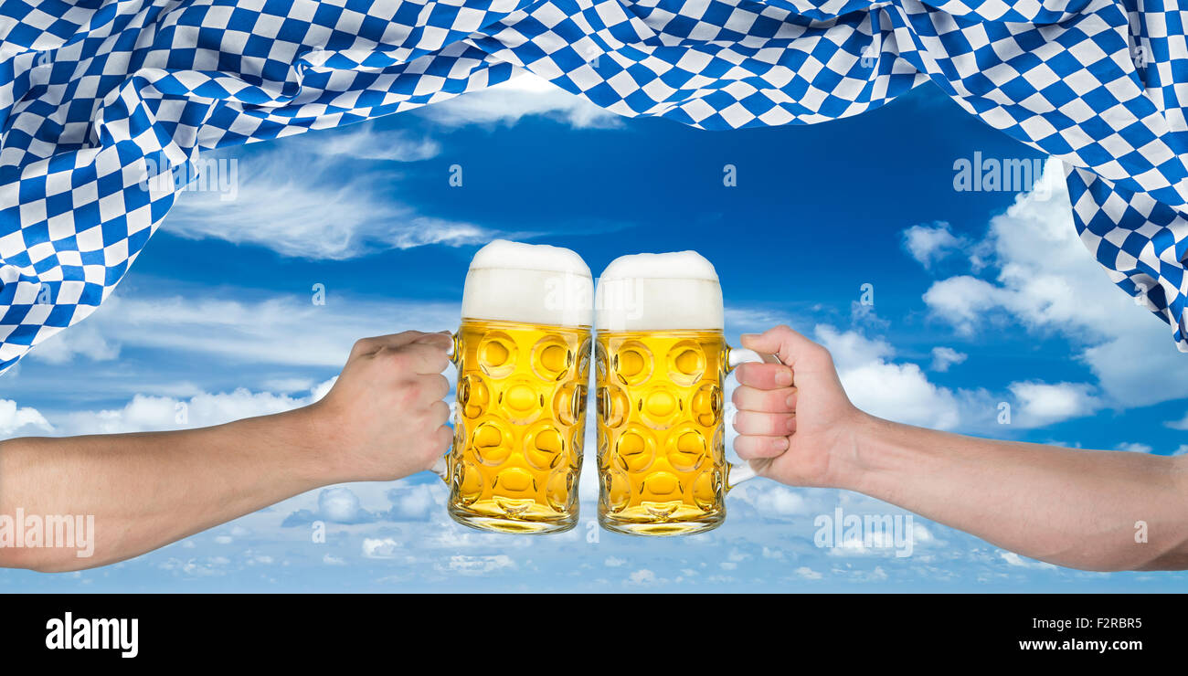 Cheers! Mani azienda tedesca a boccali da birra sotto bandiera bavarese Foto Stock