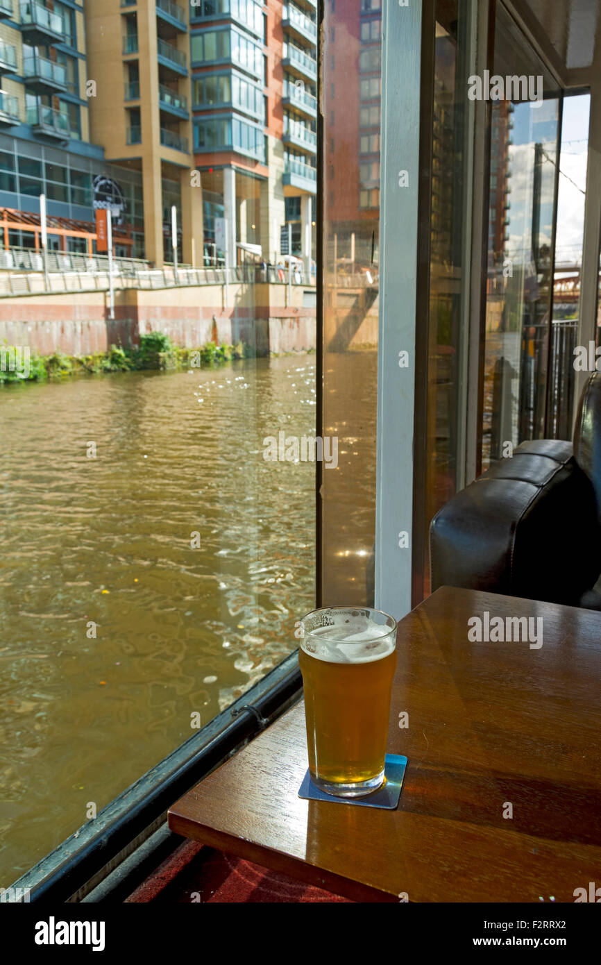 Il fiume Irwell dall'interno del Mark Addy pub, Salford, Manchester, Inghilterra, Regno Unito, con una pinta di birra in un bicchiere in primo piano Foto Stock