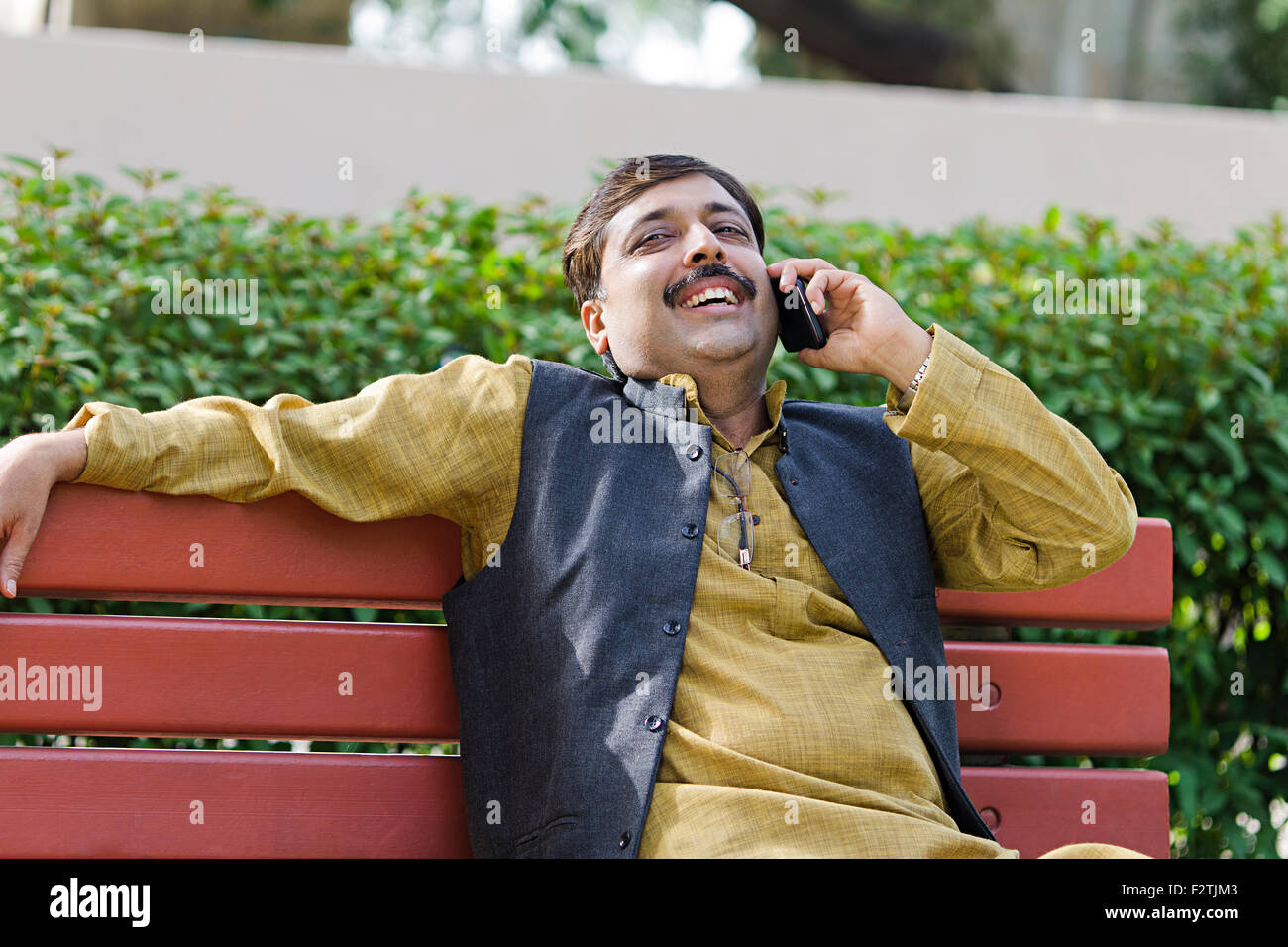 1 indian uomo adulto parco banco seduta parlando del telefono mobile Foto Stock