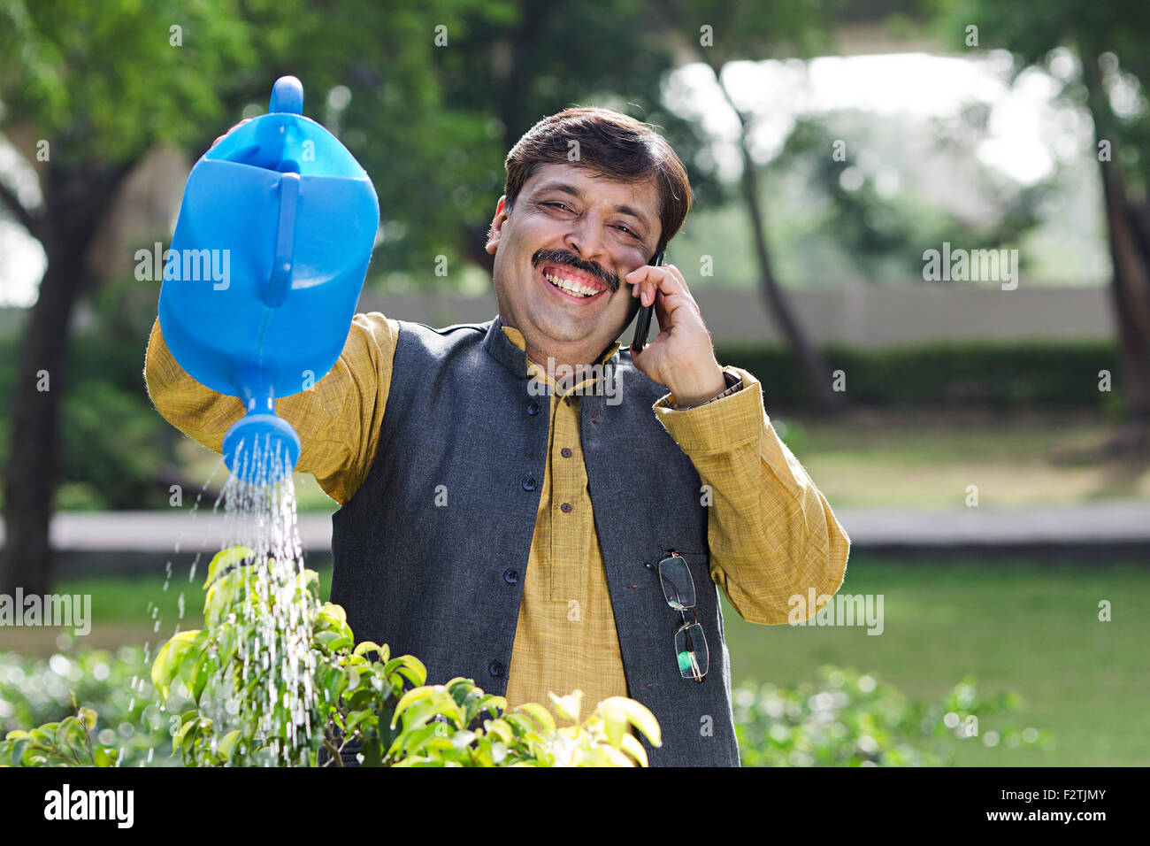 1 indian uomo adulto giardino irrigazione di piante e parlare per telefono cellulare Foto Stock