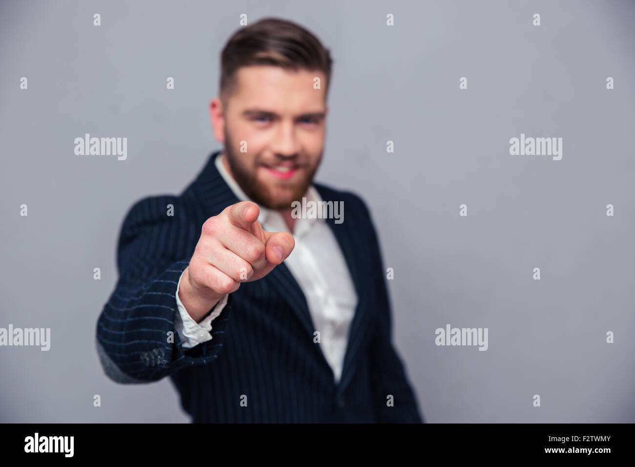 Ritratto di un imprenditore puntare il dito in telecamera su sfondo grigio. La messa a fuoco a portata di mano Foto Stock