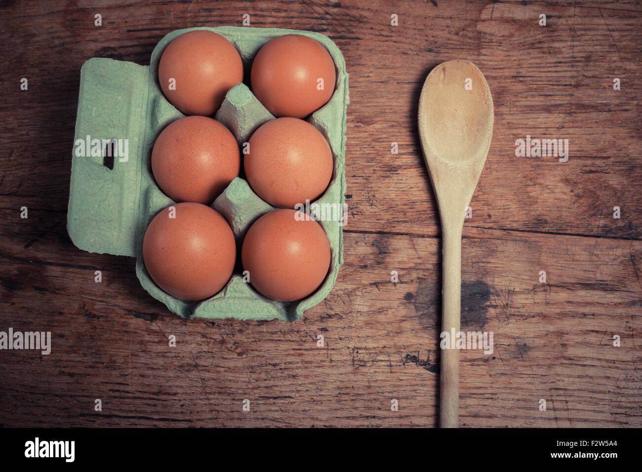 Uova e un cucchiaio di legno su una tavola di legno Foto Stock