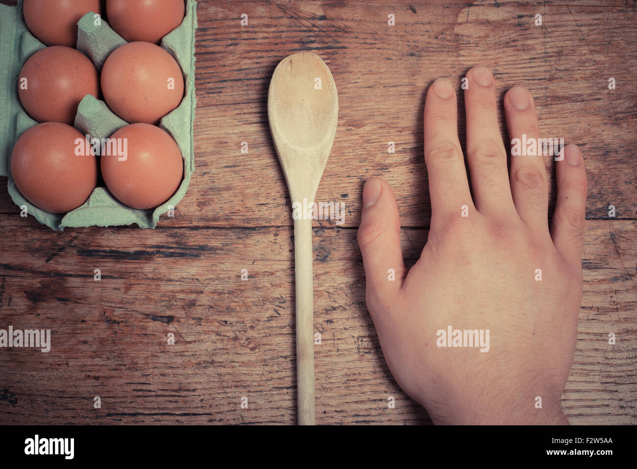 Uomo appoggiato la sua mano accanto alle uova e un cucchiaio di legno su un tavolo Foto Stock