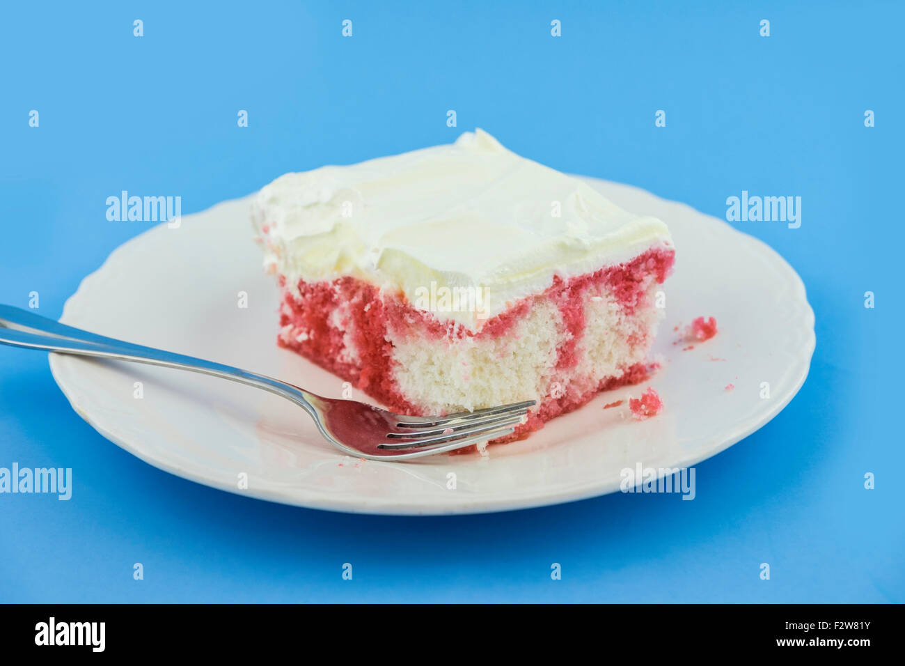 Un pezzo di torta soda-pop fatta in casa su un piatto dessert bianco su uno sfondo blu. Fatto con soda fragola, jello fragola. STATI UNITI. Foto Stock