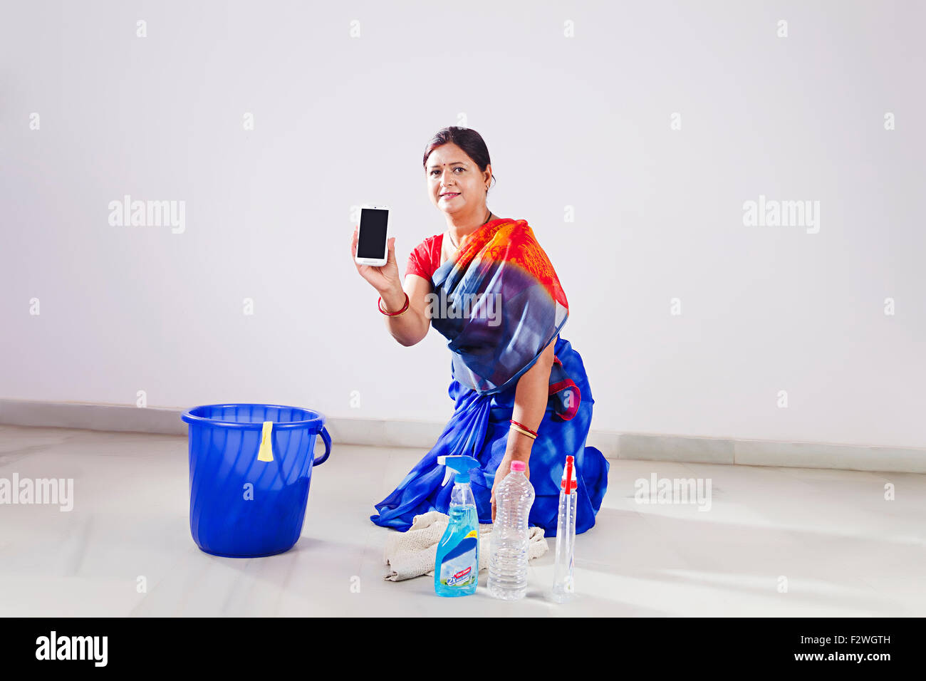 1 Adulto indiano donna casalinga pulizia di pavimenti e mobili di qualità telefono mostra Foto Stock