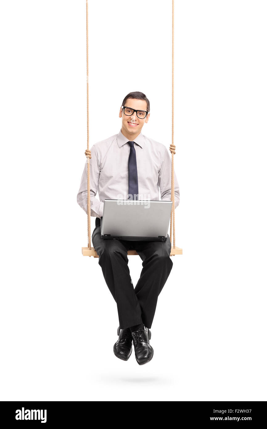 Colpo verticale di una gioiosa giovane imprenditore lavora su un laptop seduto su una oscillazione in legno isolato su sfondo bianco Foto Stock