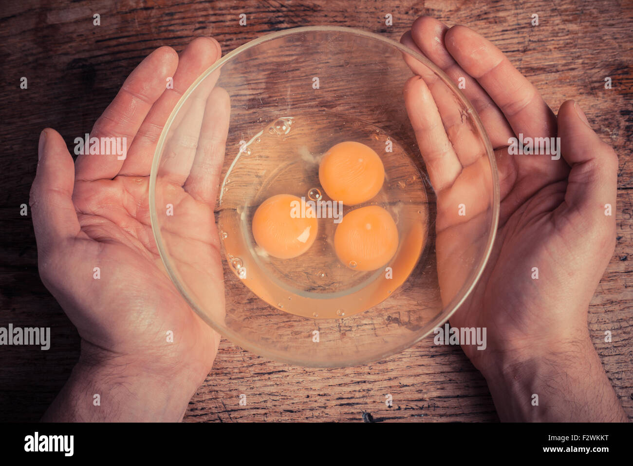 Mani tenendo una ciotola con tre uova crude in esso Foto Stock