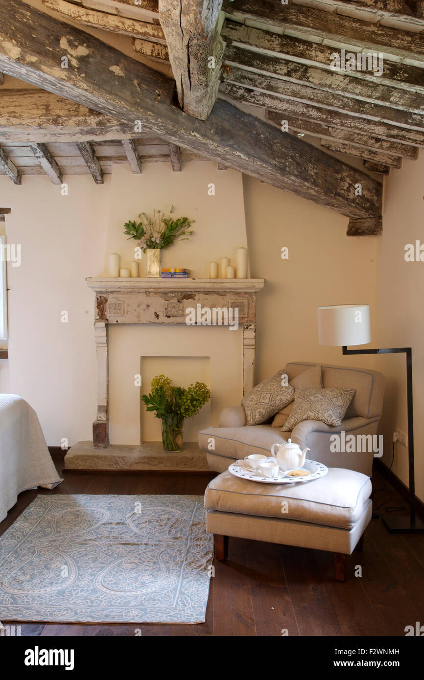 La crema Poltrona e pouf in paese italiano en camera in stile rustico con soffitto con travi in legno a vista Foto Stock