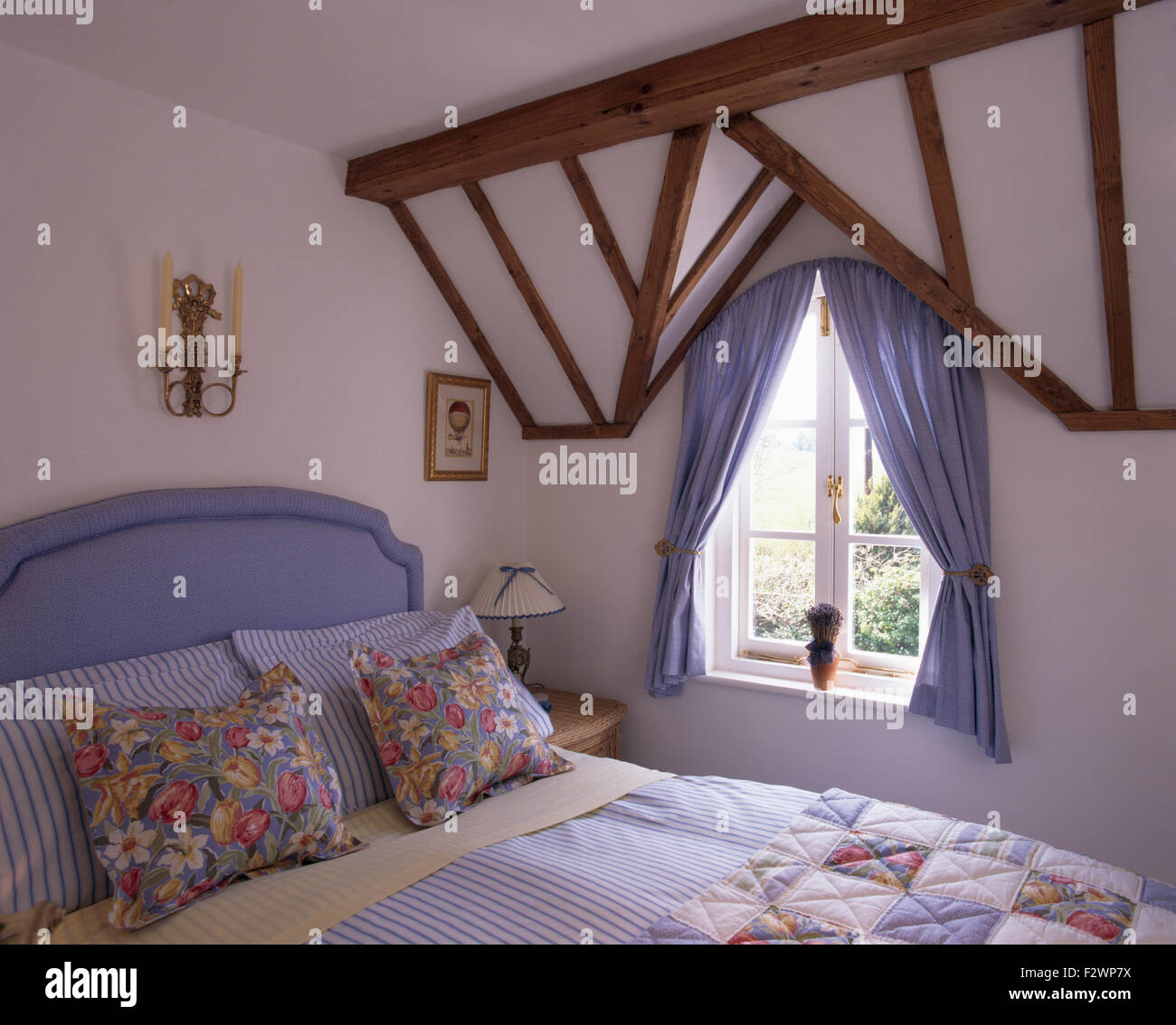 Cuscini floreali blu sul letto imbottito in paese camera da letto con un pallido tende blu su windows Foto Stock