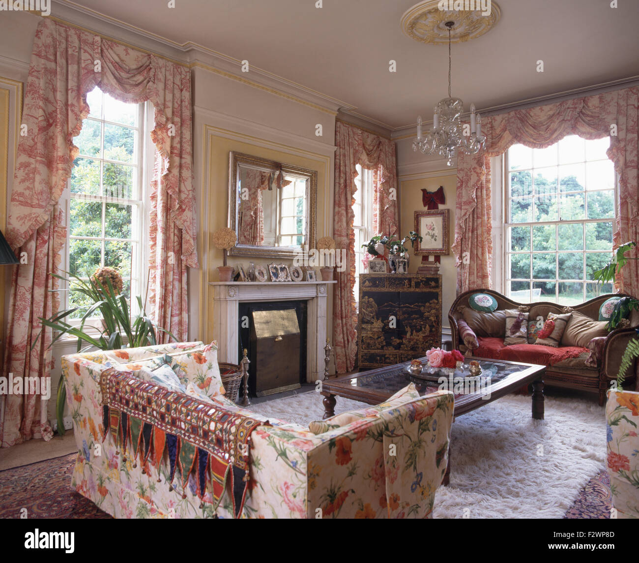 Indian buttare su un divano floreale in un paese degli anni novanta soggiorno con Toile de Jouy tende su windows Foto Stock