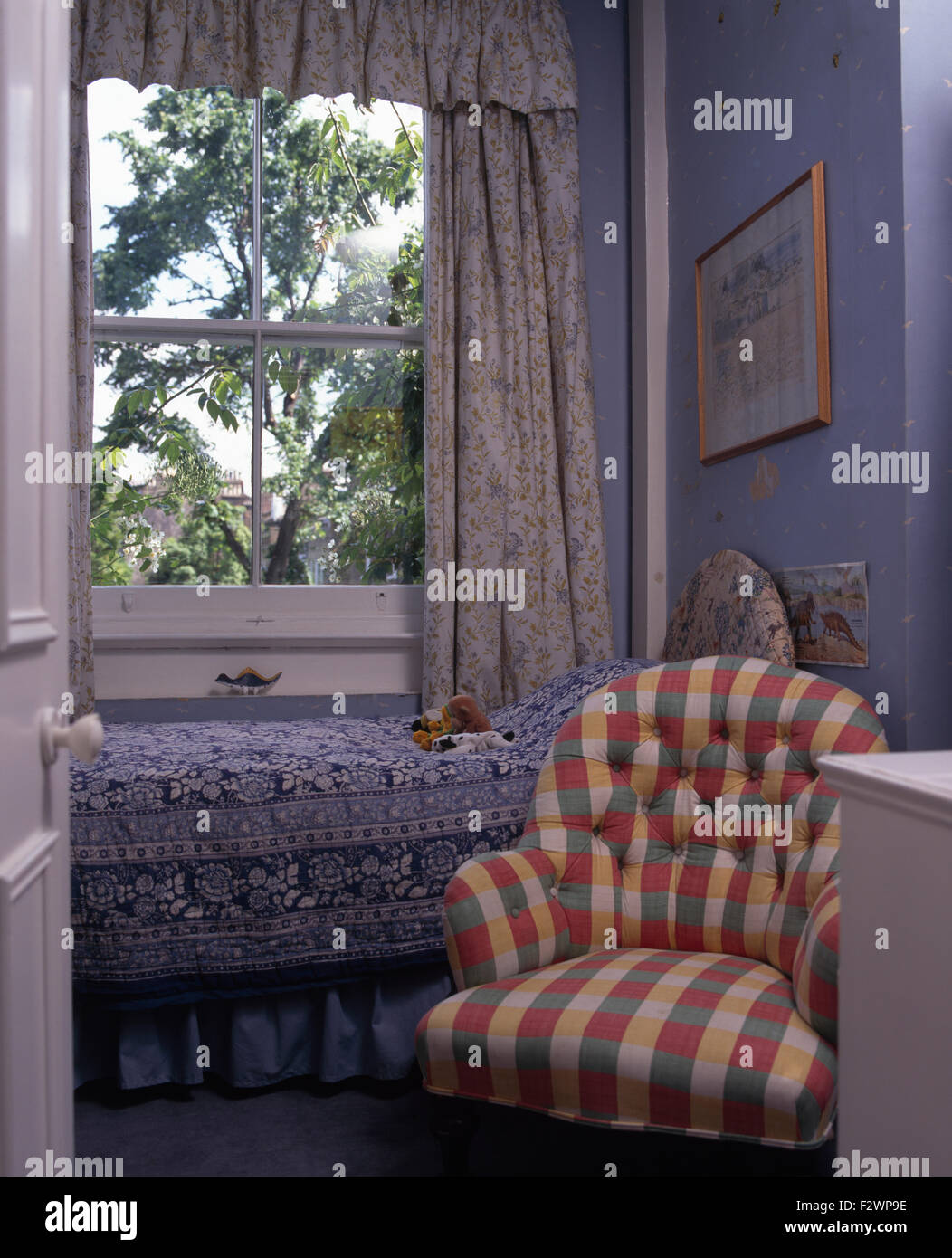 Controllato da pulsante Indietro sedia in blu piccola camera da letto con letto singolo sotto la finestra con tende dai motivi floreali Foto Stock