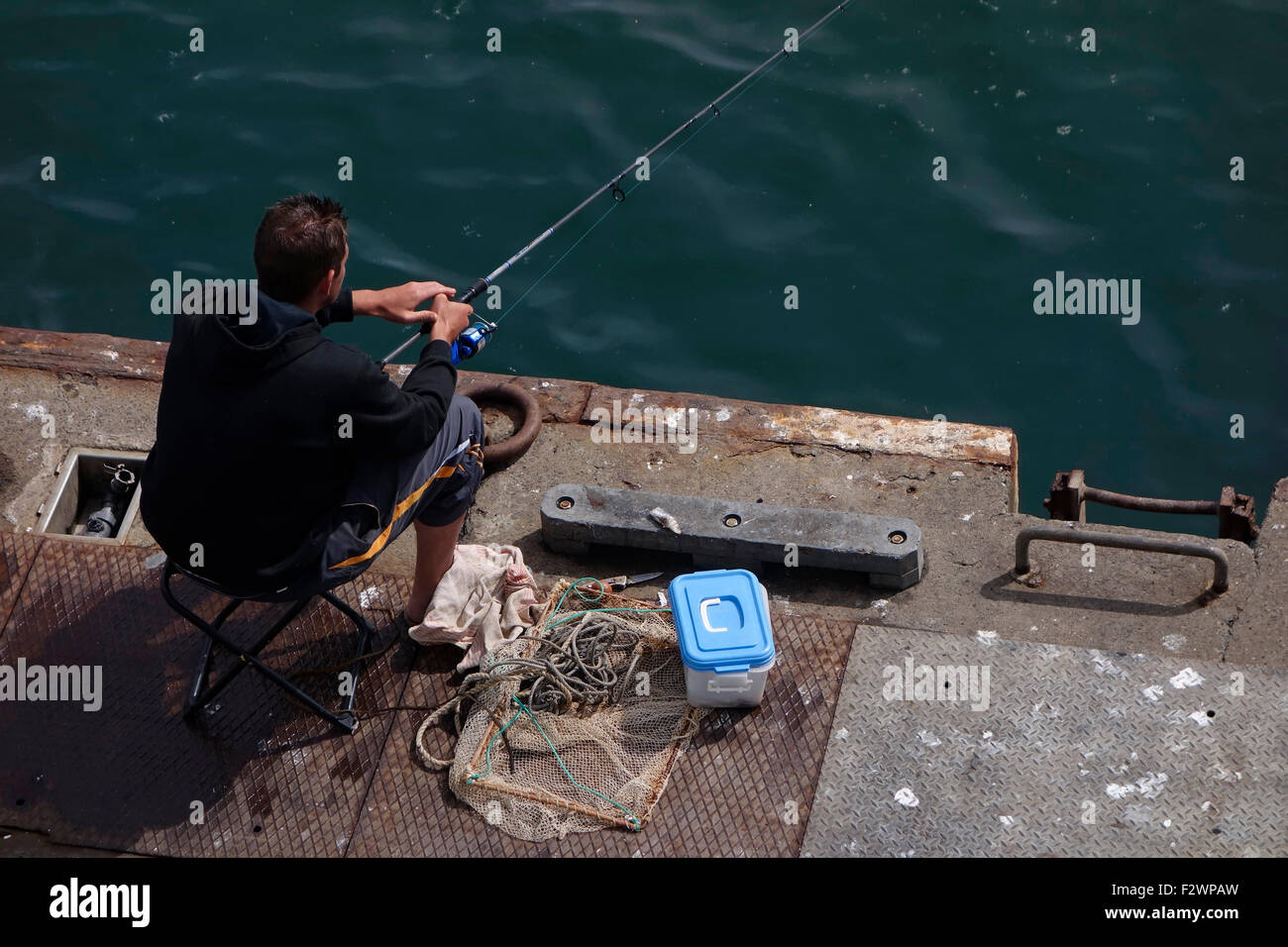 Il pescatore / pescatore con canna da pesca per la cattura di pesce dalla banchina di Porto Foto Stock