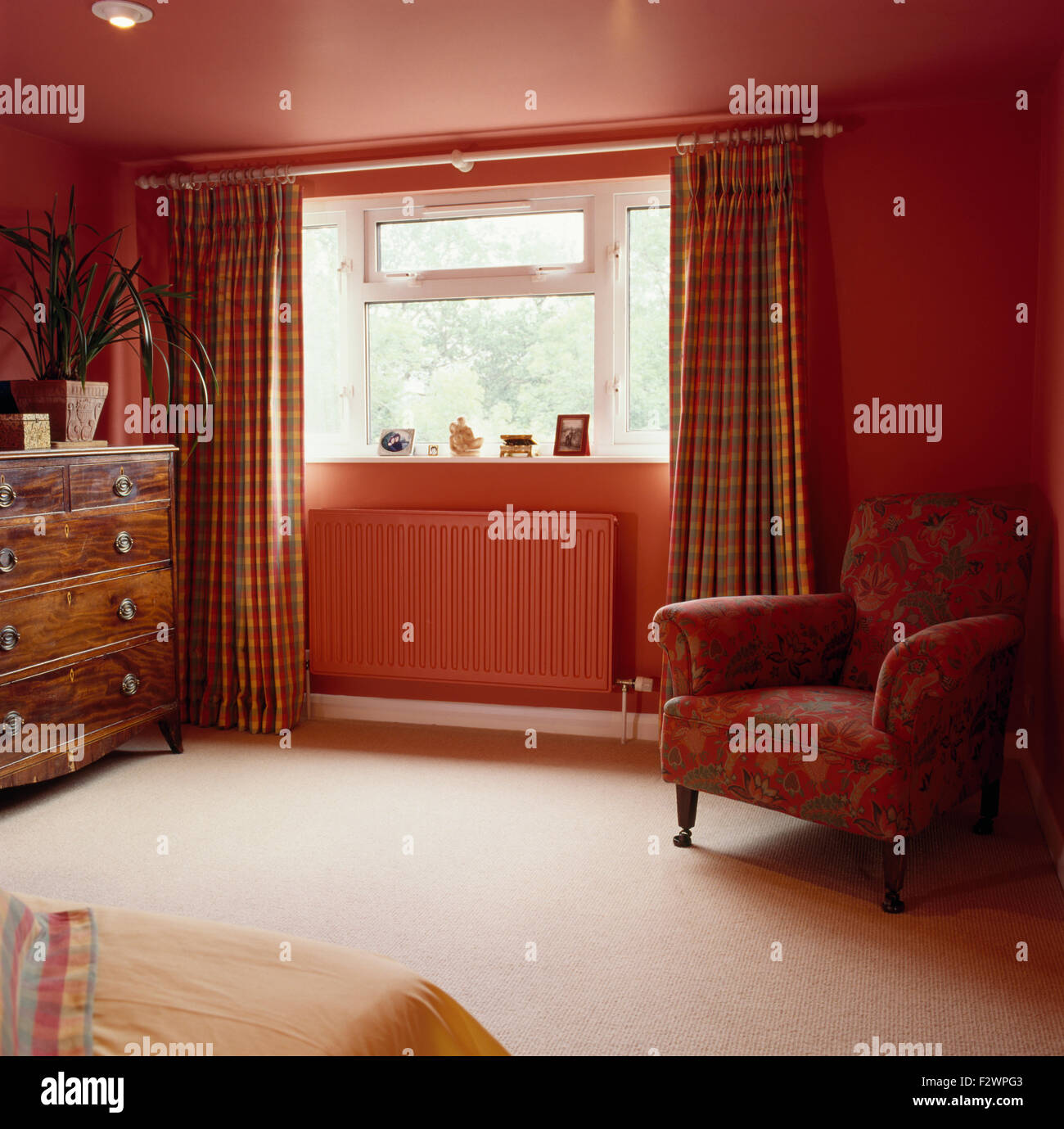 Controllato tende su finestra sopra radiatore verniciato in rosso degli anni novanta camera con moquette color crema e rosso sedia Foto Stock