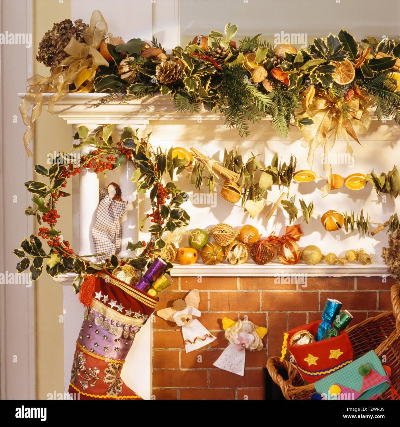 Fatto in casa ghirlanda di frutta e holly corona sul camino con una seta colorata calza di Natale Foto Stock