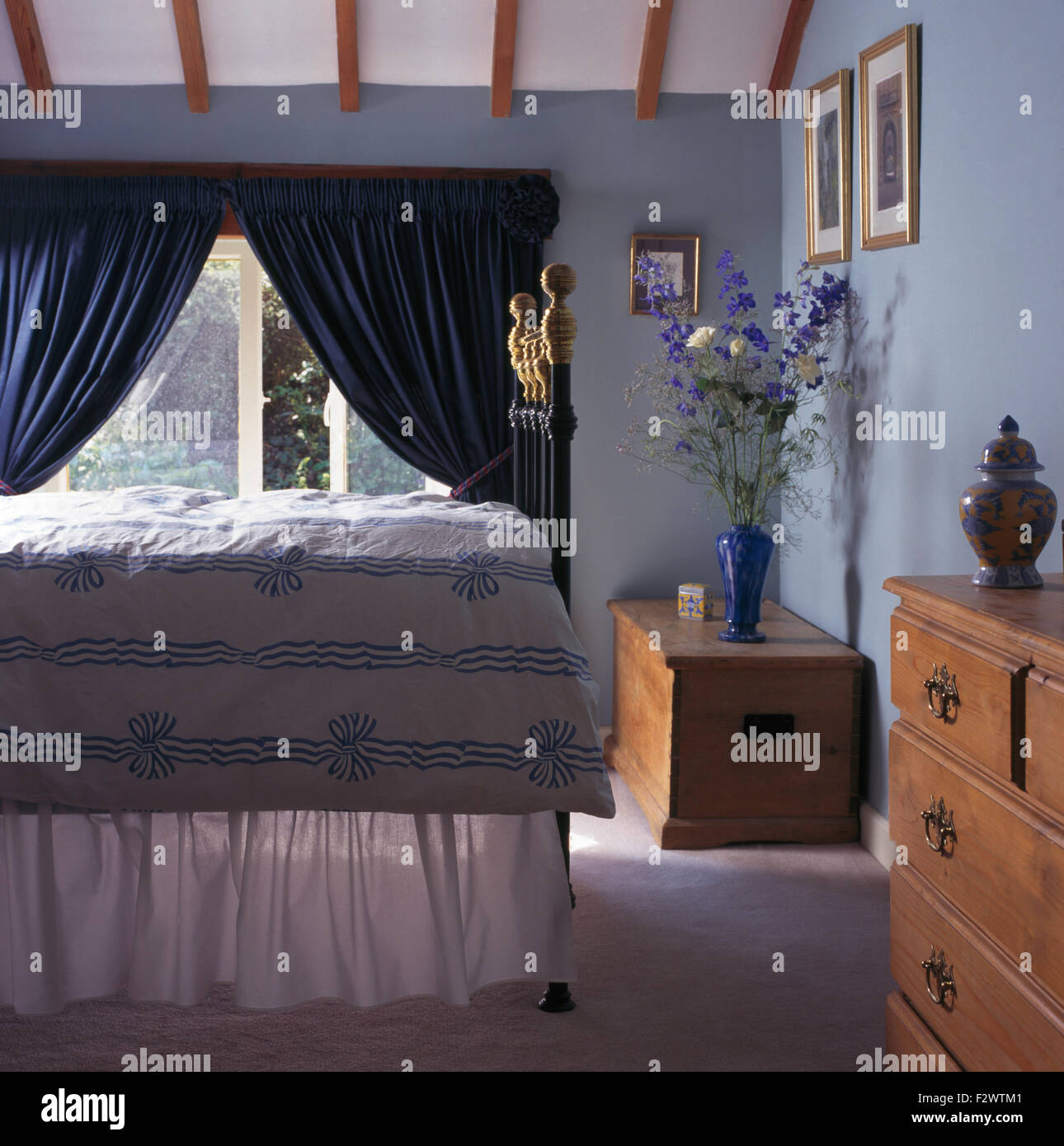 Blue+nastro bianco piumino modellato su ottone letto in camera da letto degli anni novanta con blu scuro tende sulla finestra Foto Stock