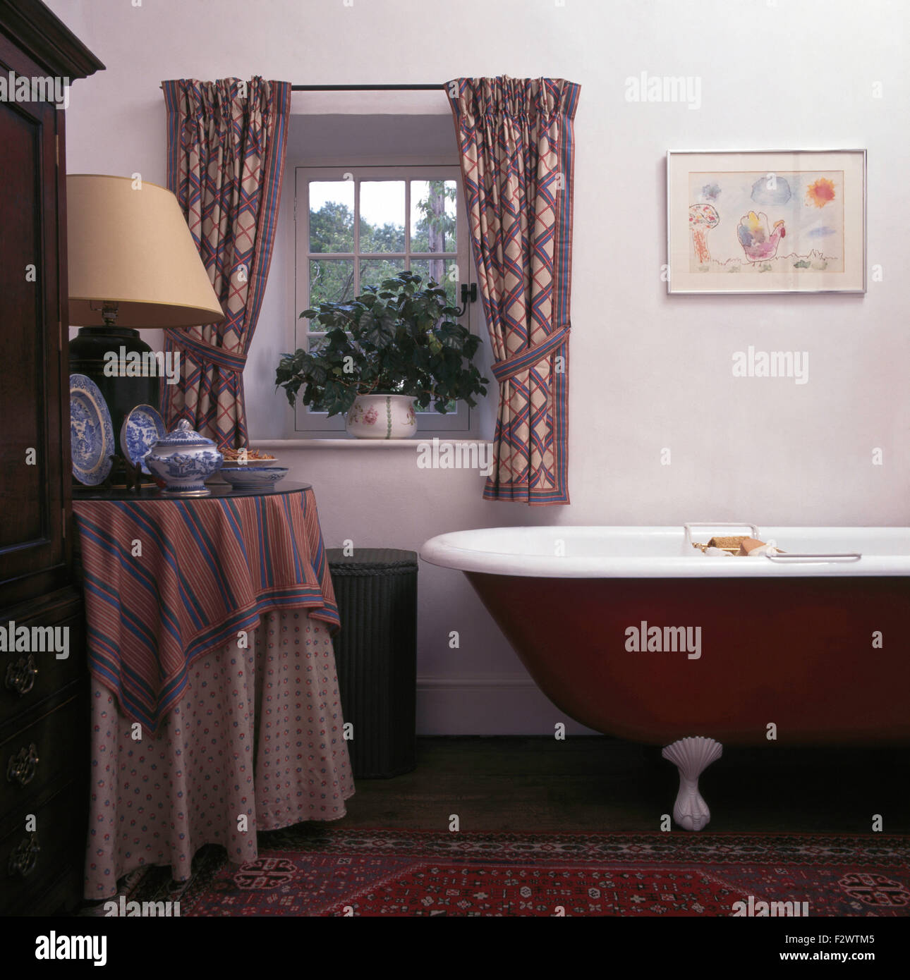 Tende a motivi geometrici su piccola finestra sopra brown roll top bagno degli anni novanta in bagno cottage Foto Stock