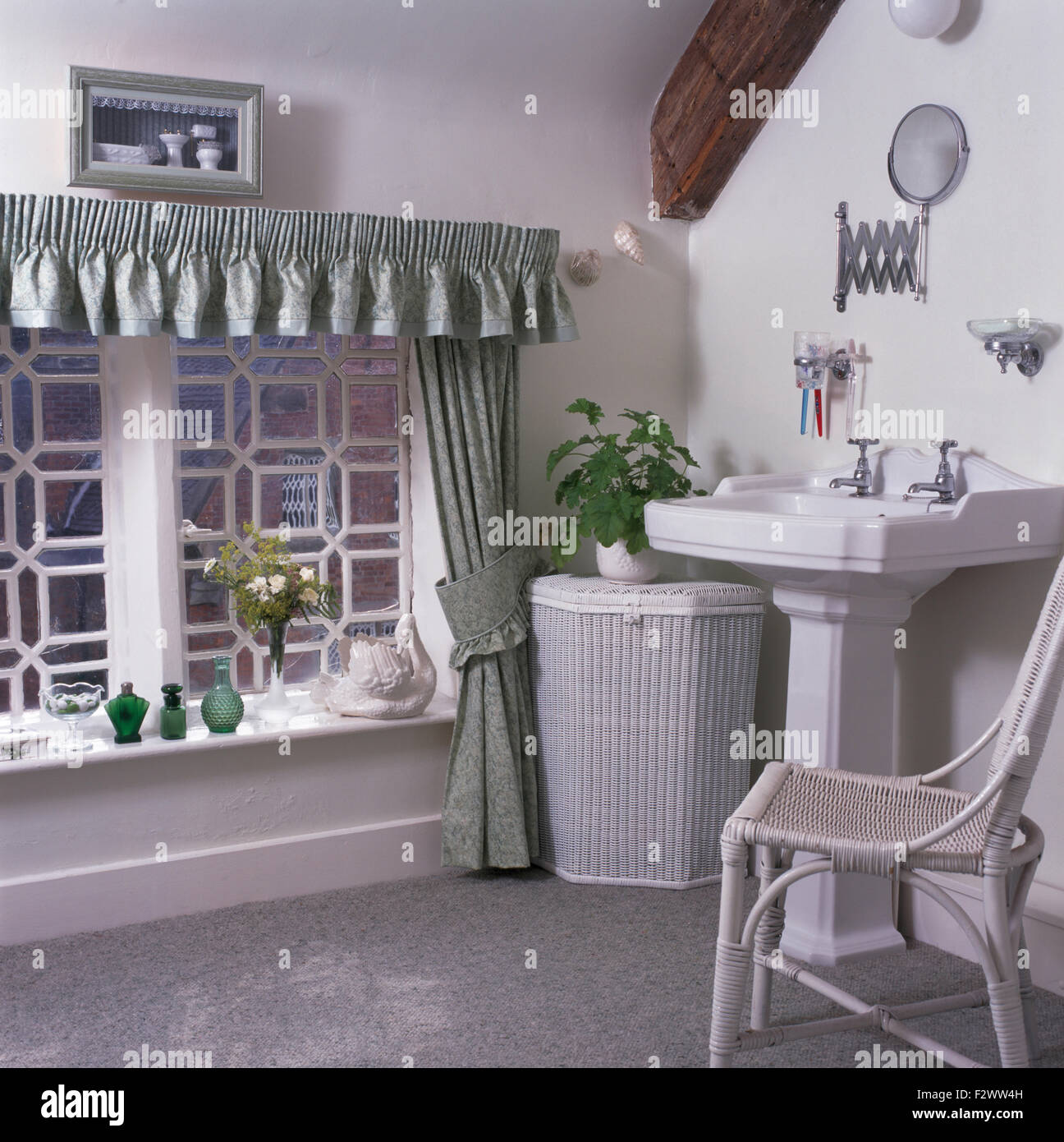 Dipinto di bianco vimini cesto per la biancheria e sedia in bianco cottage bagno con verde pallido tende sulla finestra Foto Stock