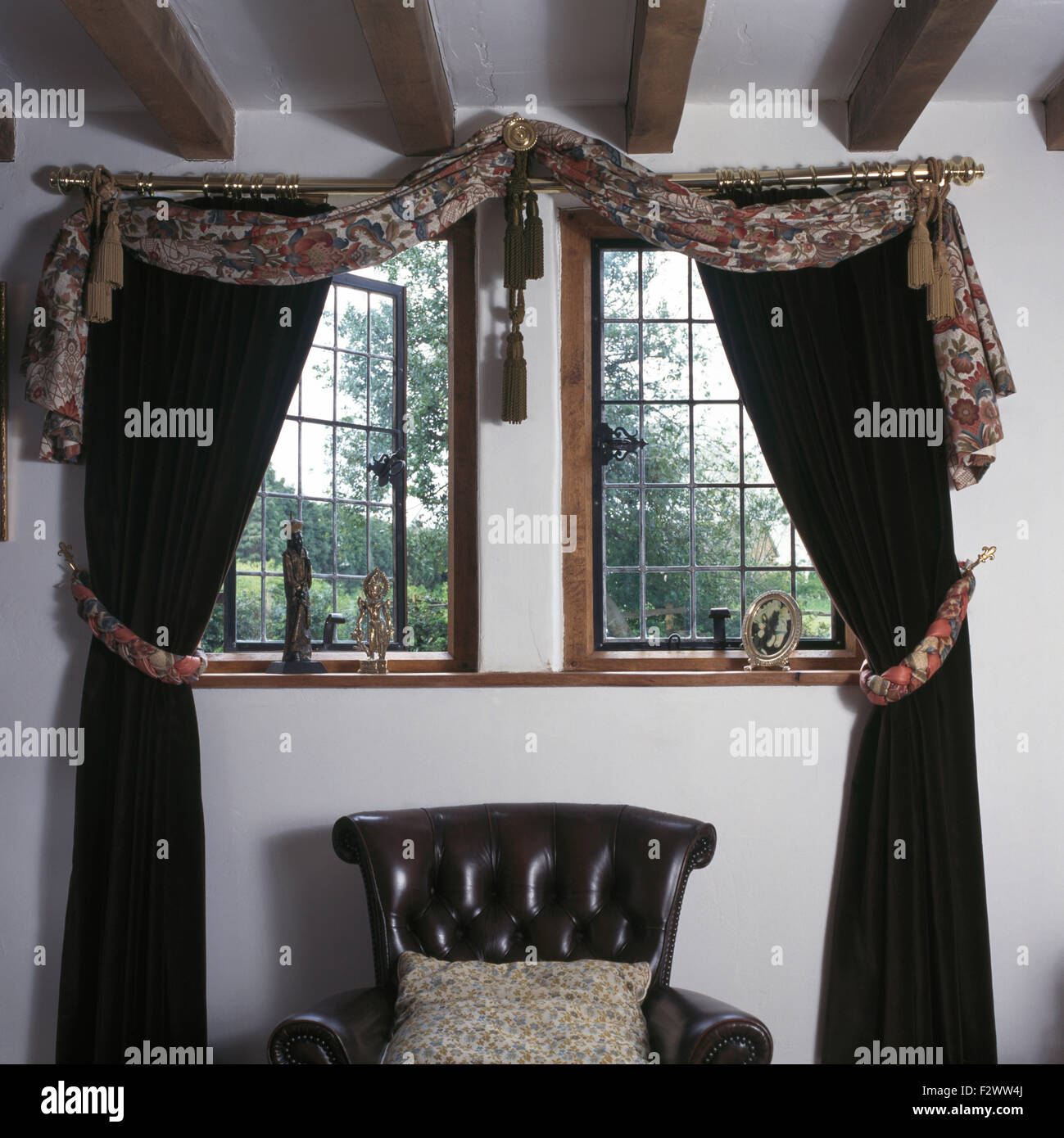 Tessuto drappeggiato e tende nere sulla finestra di reticolo nero sopra la sedia di cuoio degli anni novanta in camera da letto Foto Stock